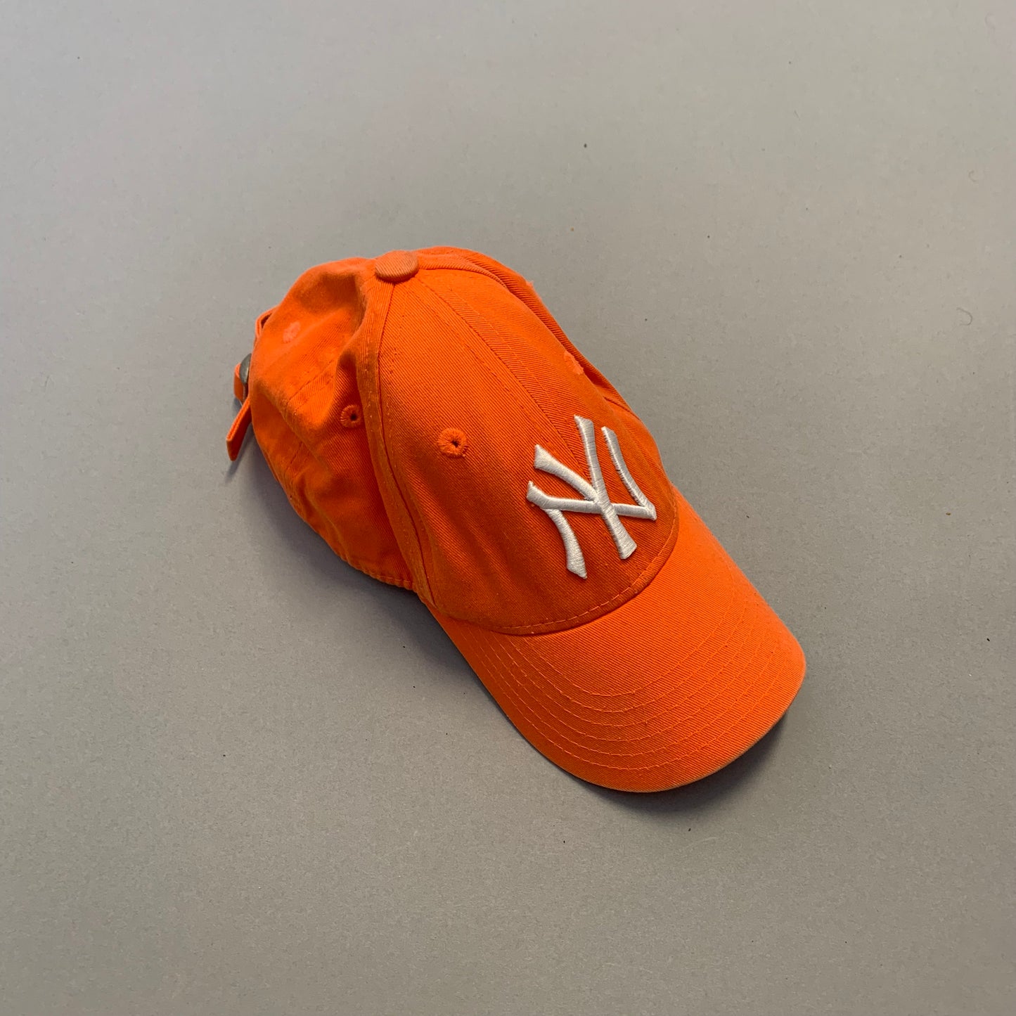 Orange baseball cap with white logo on a gray background.