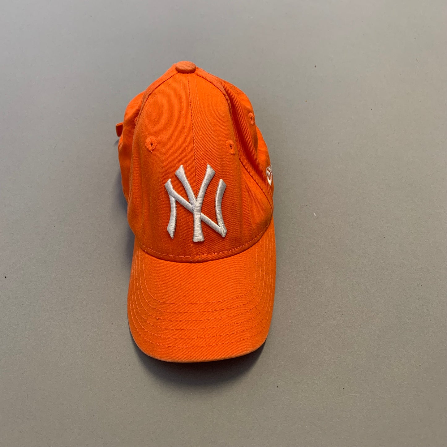 Orange baseball cap with white nullNYnull logo on a gray surface.