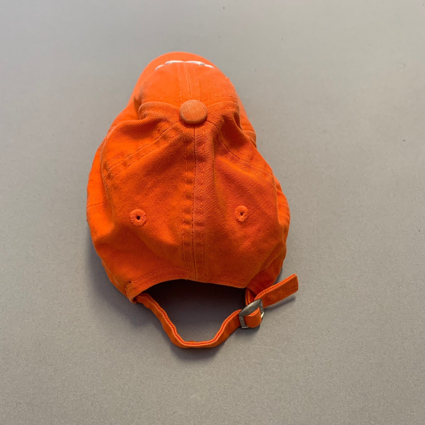 Orange baseball cap with strap on a gray background.