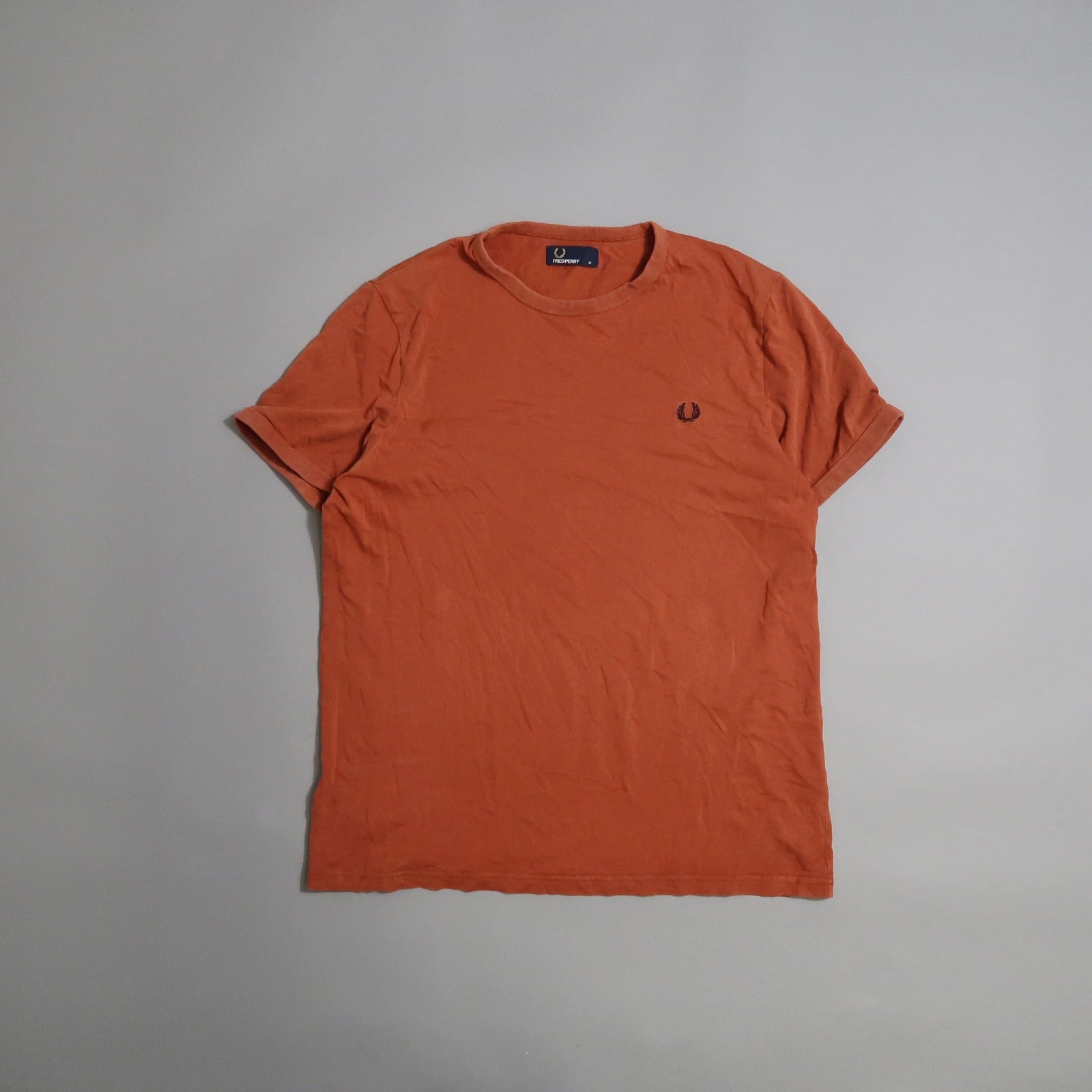 Wrinkled orange T-shirt with embroidered emblem on the chest.