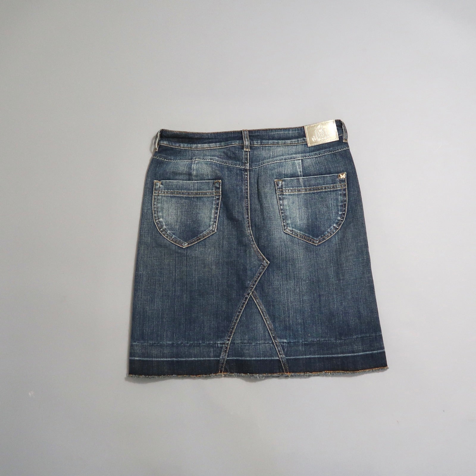 Denim skirt with back pockets on a plain gray background.