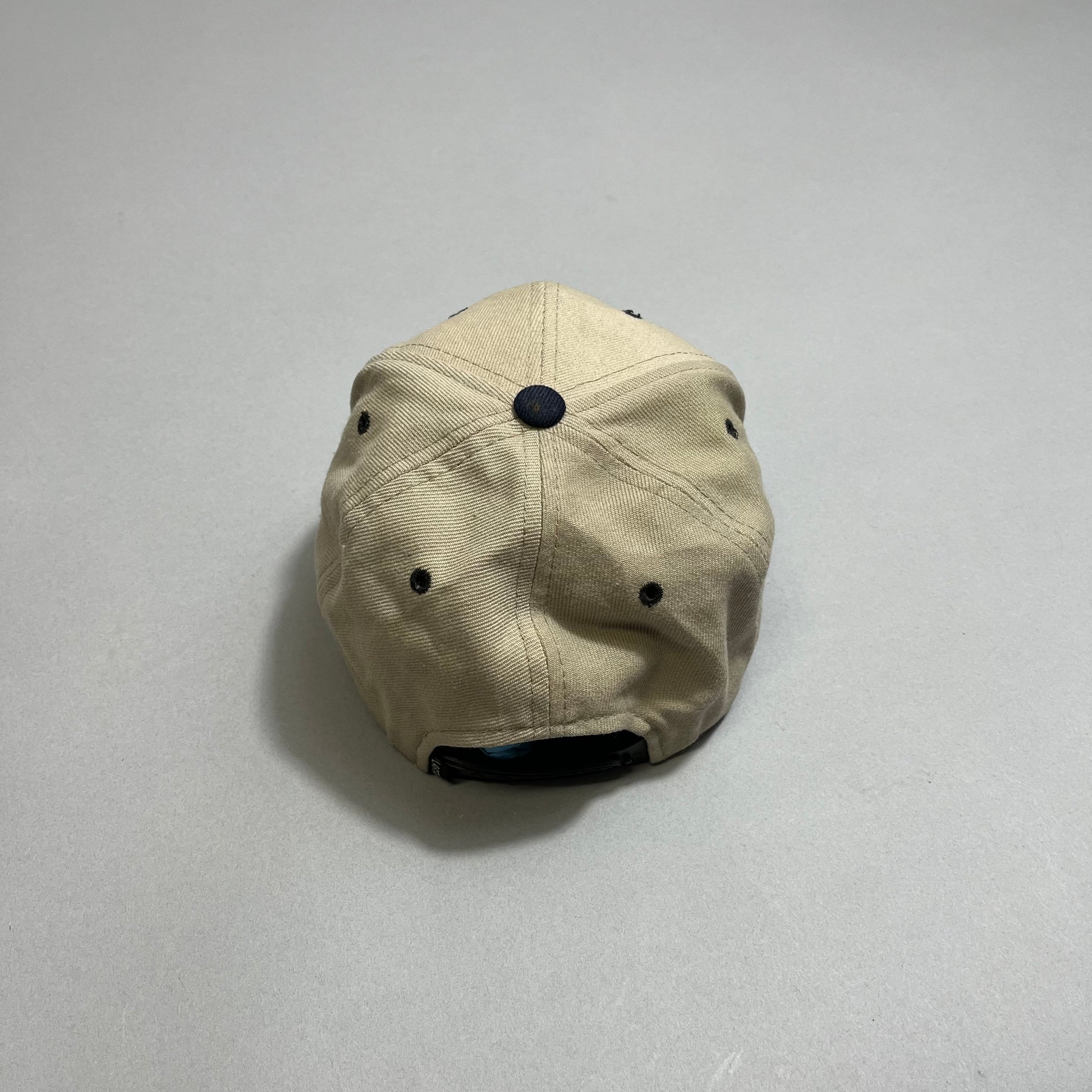 A beige cap with black eyelets and top button, viewed from the back.