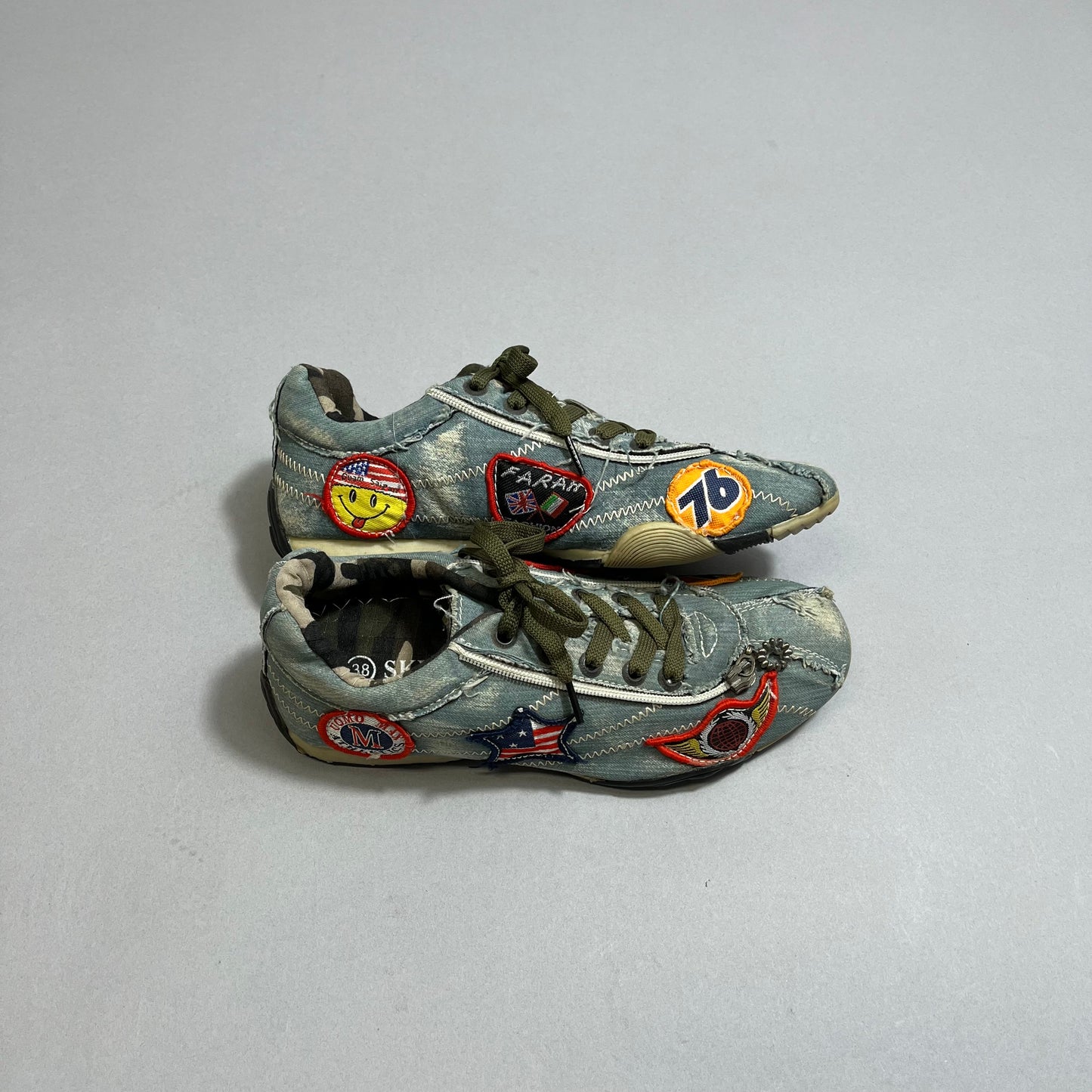 Worn denim sneakers with colorful patches on a gray surface.