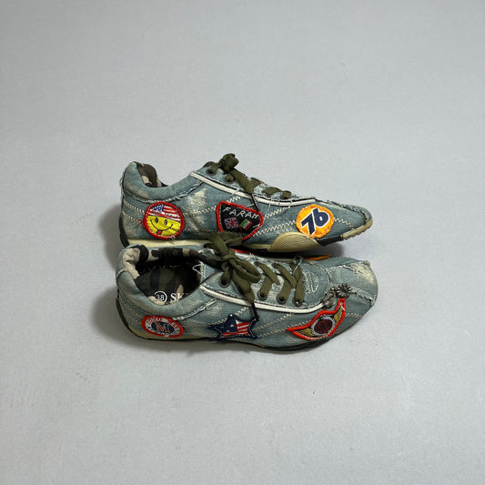 Worn denim sneakers with colorful patches on a gray surface.