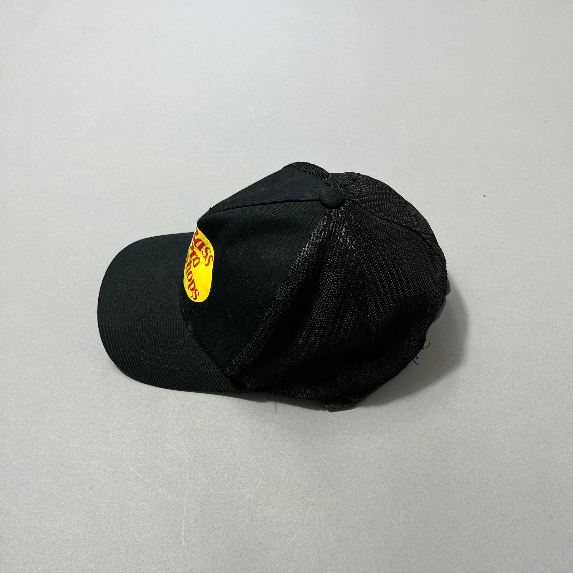 Black cap with yellow and red logo, resting on a gray surface.