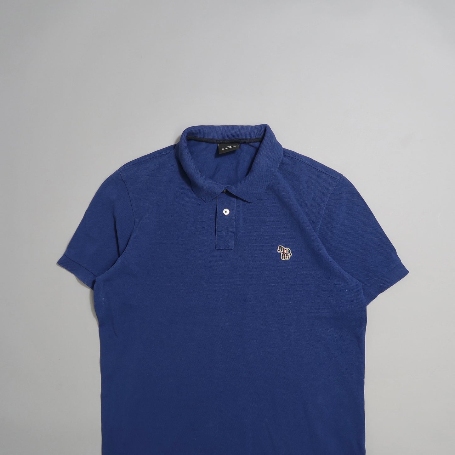 Blue polo shirt with small embroidered logo on a gray background.