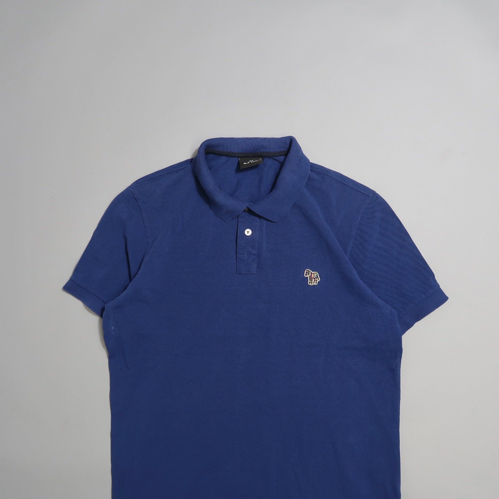 Blue polo shirt with small embroidered logo on a gray background.