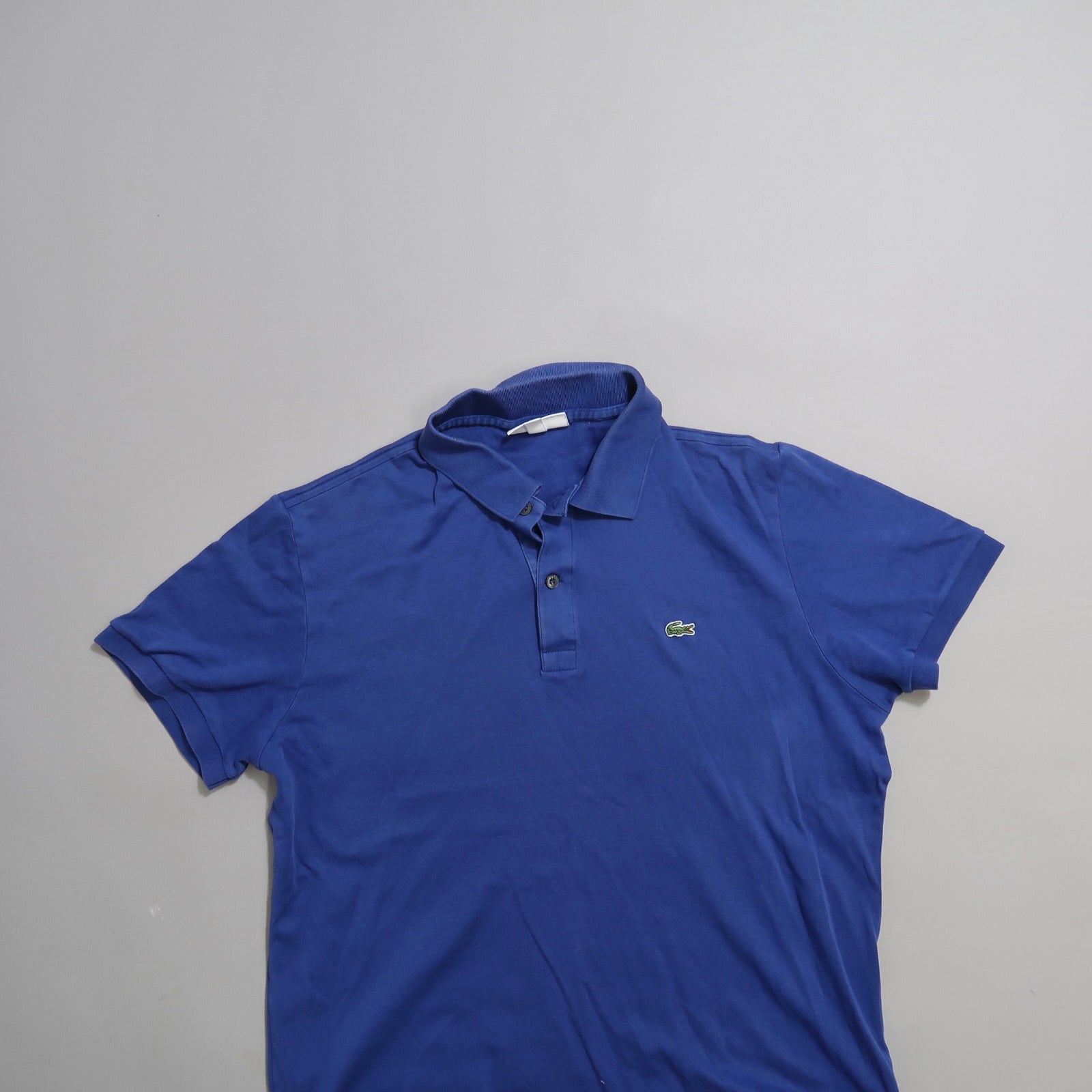 Blue polo shirt with a green logo on a plain gray background.