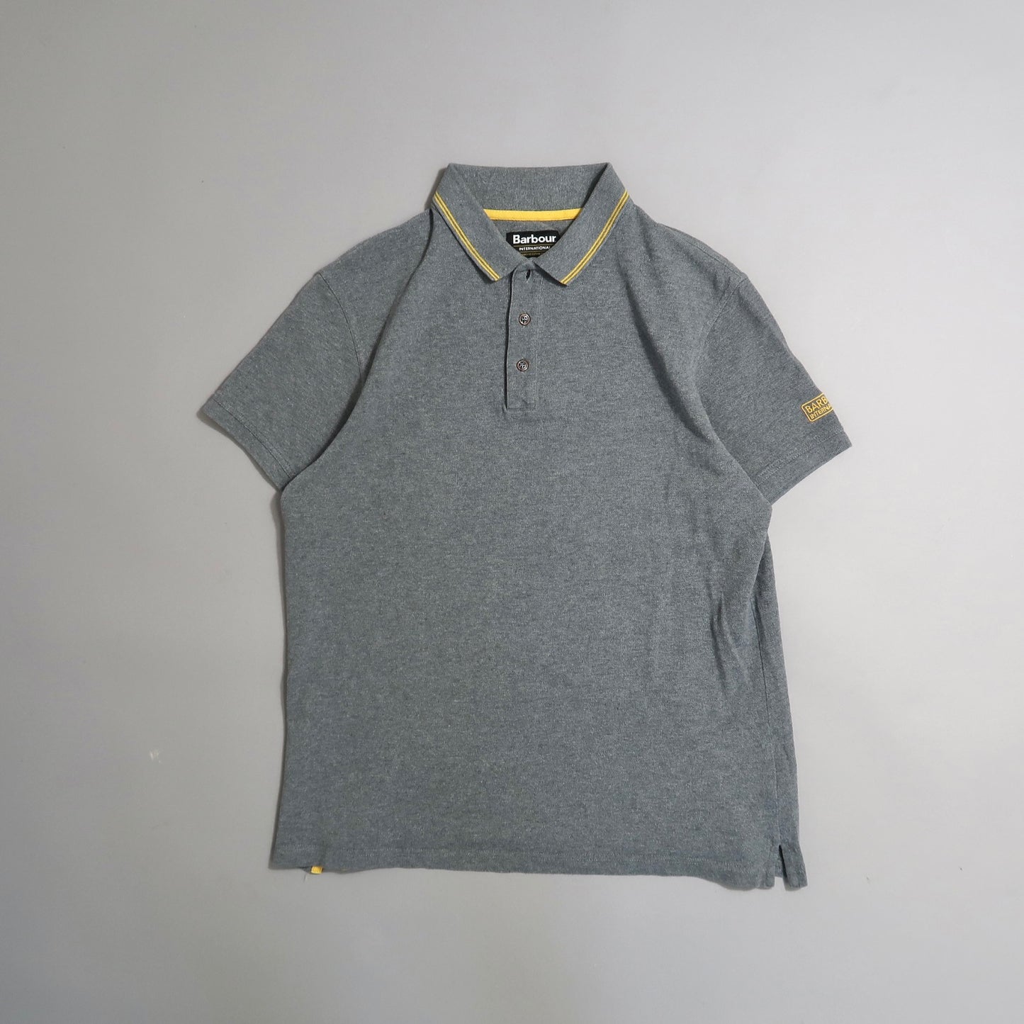 Gray polo shirt with yellow striped collar detail, laid on a flat surface.