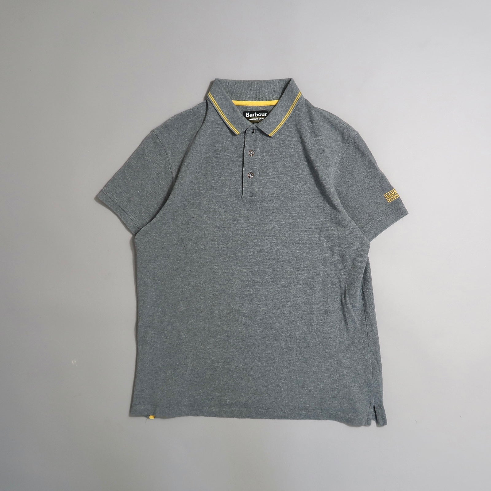 Gray polo shirt with yellow striped collar detail, laid on a flat surface.