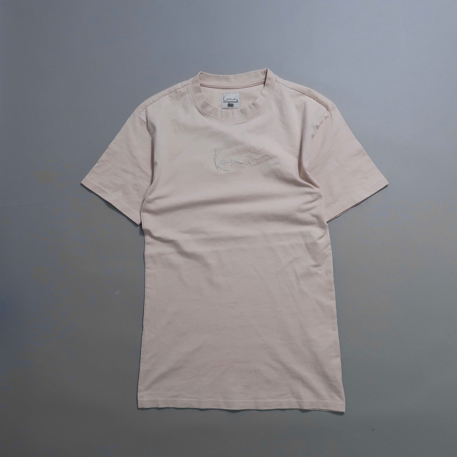 Plain beige t-shirt with embroidered design on a gray background.