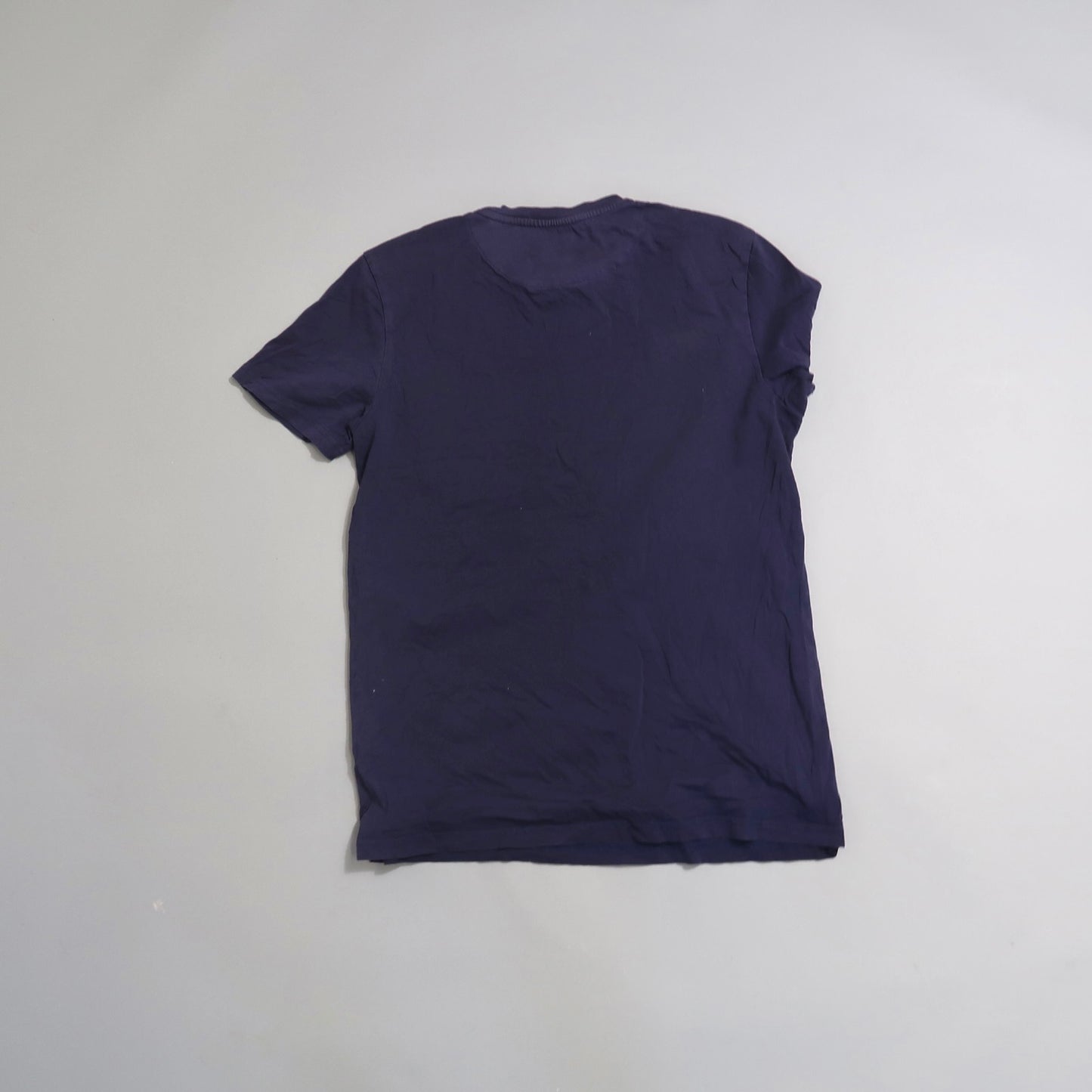 Back view of a plain navy blue T-shirt on a gray background.