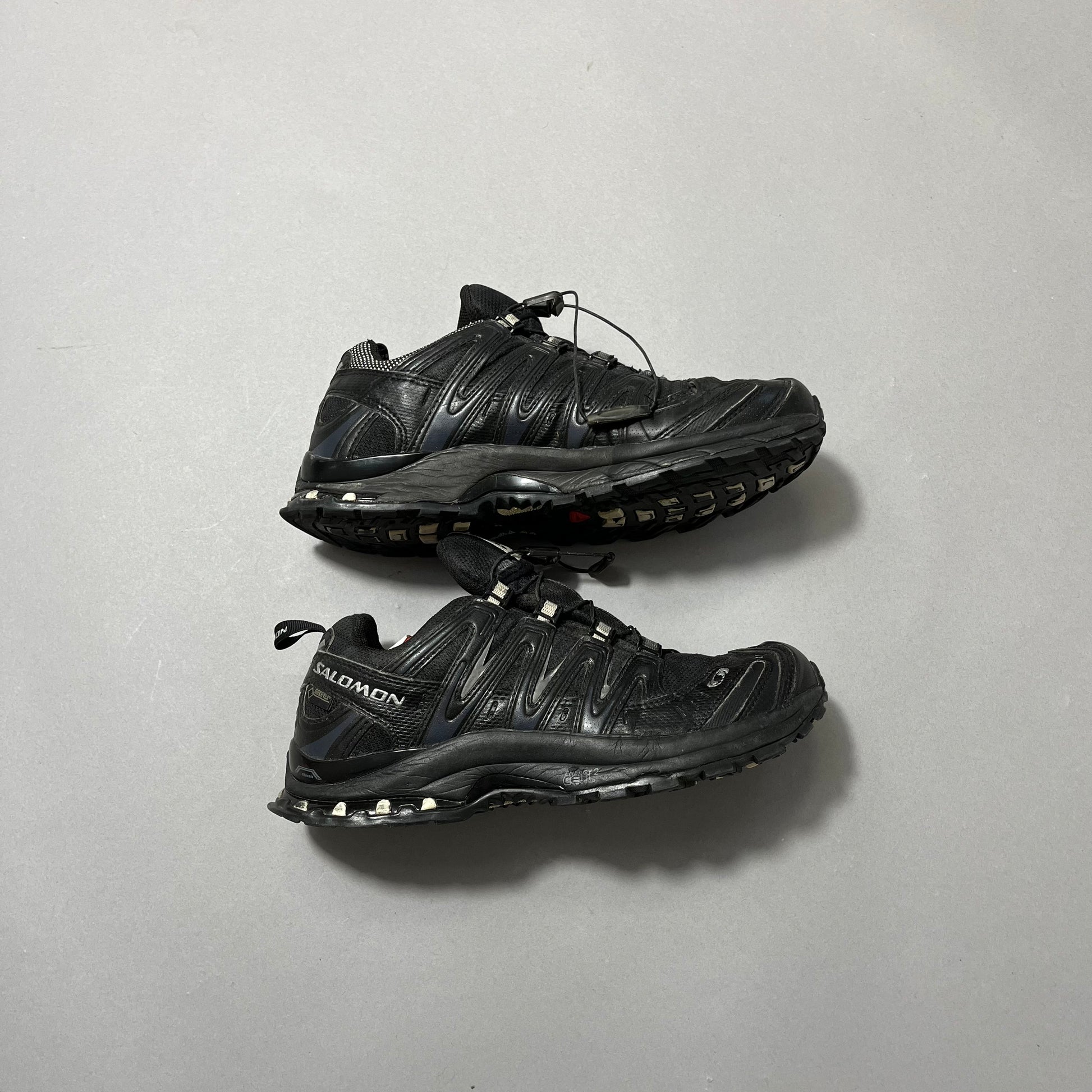 Black trail running shoes on a plain gray background.