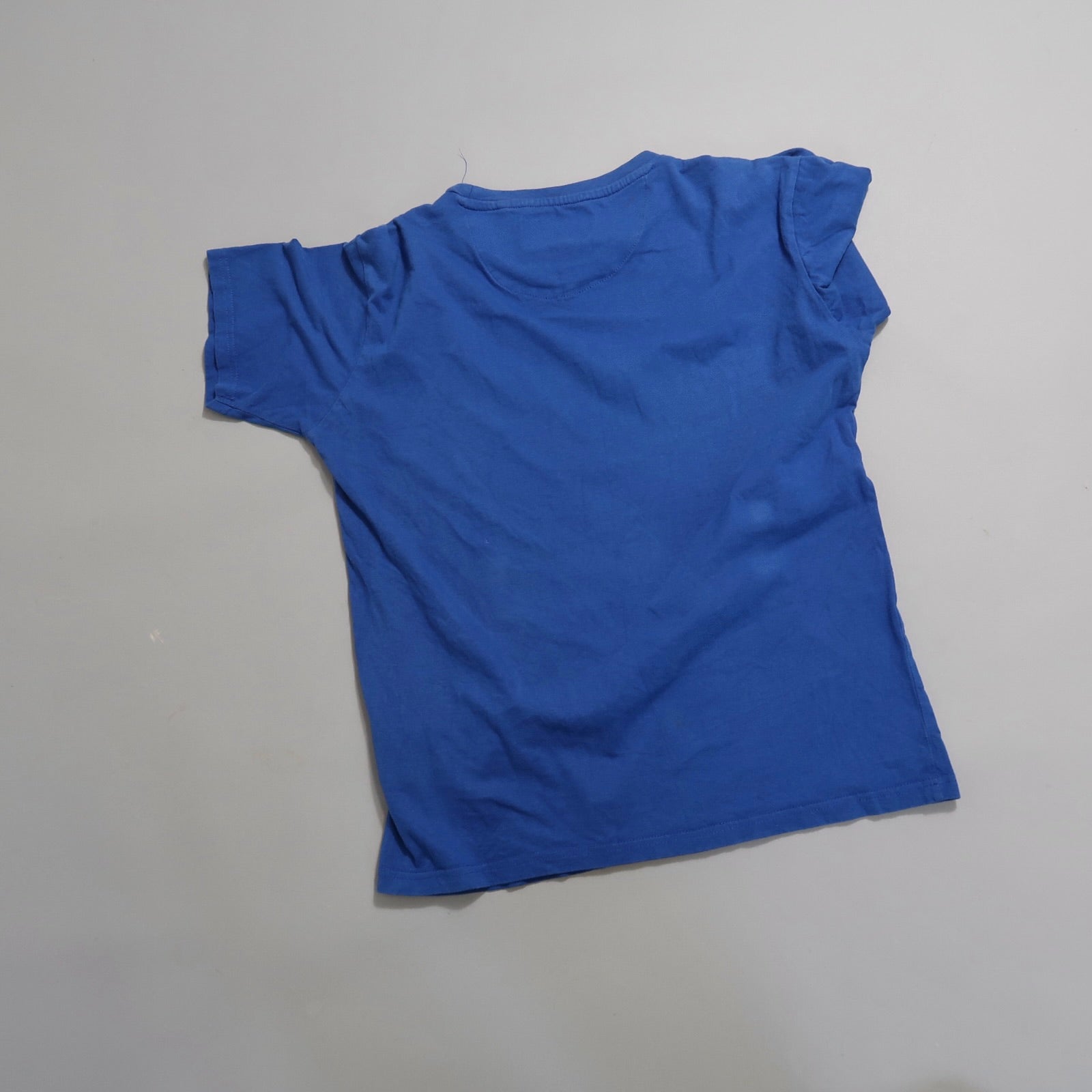 Blue T-shirt laid flat on a neutral background.