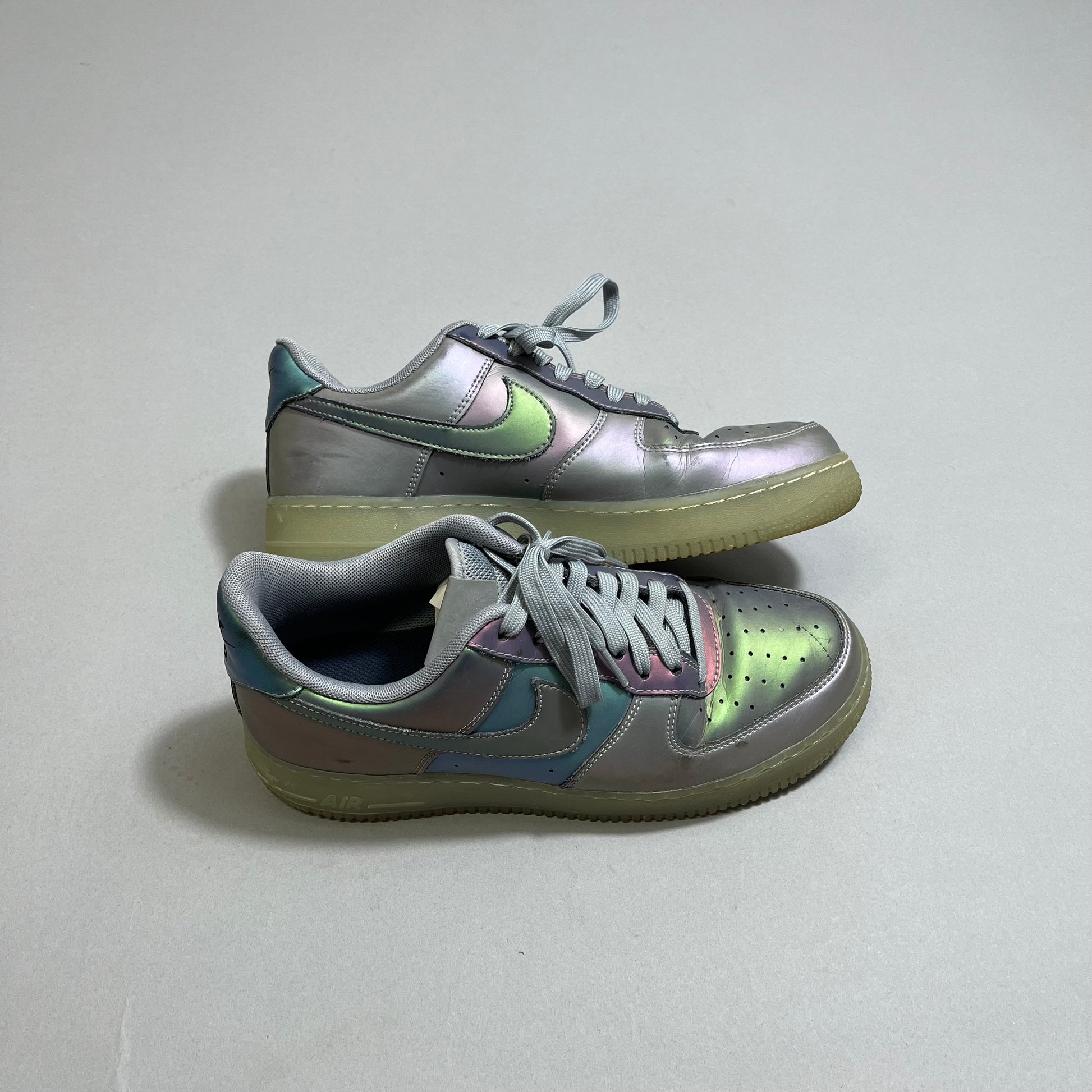 Iridescent sneakers with gray laces and gum soles on a gray surface.