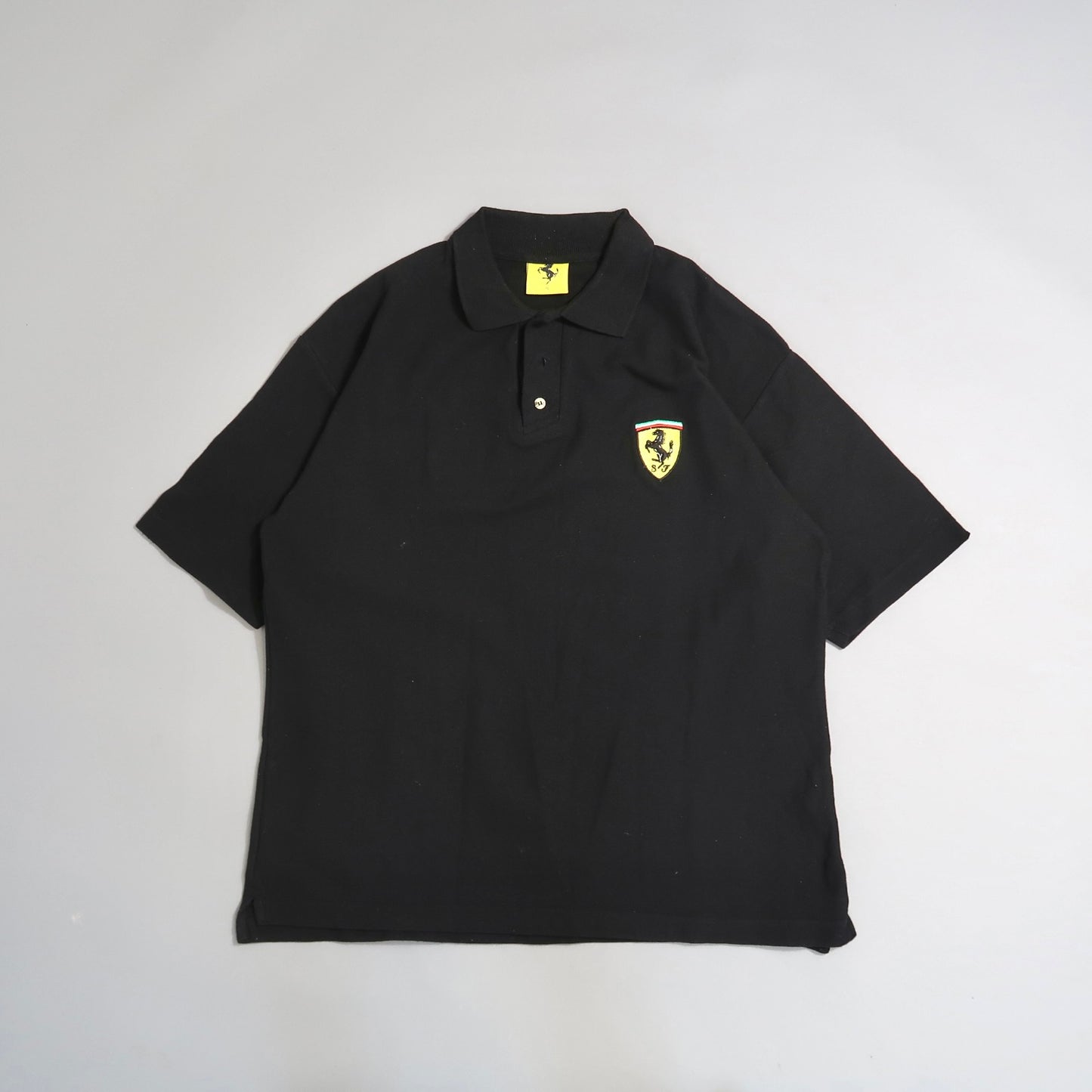 Black polo shirt with yellow Ferrari logo patch on the chest.