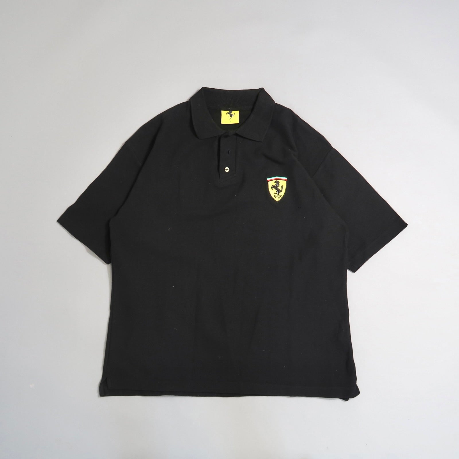 Black polo shirt with yellow Ferrari logo patch on the chest.