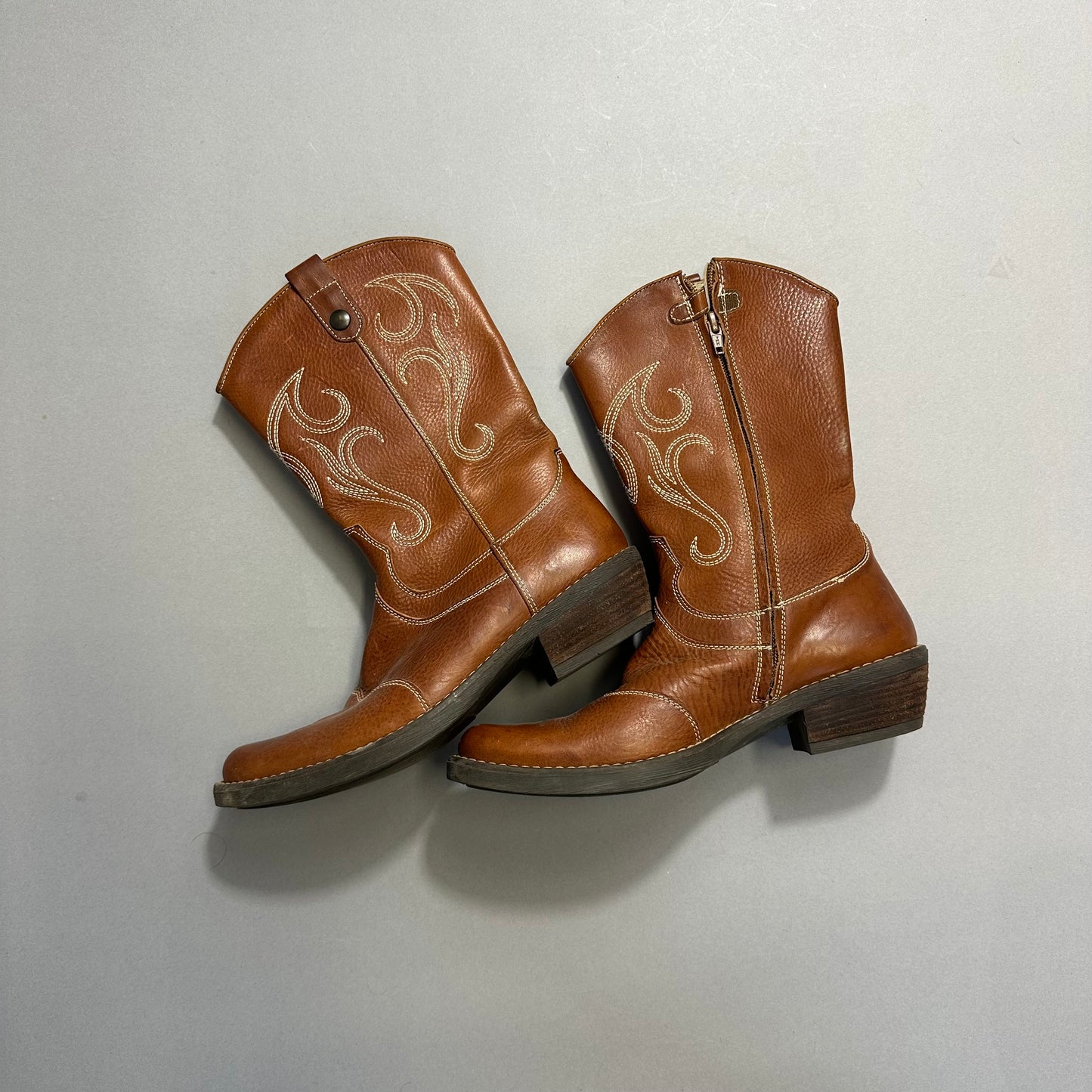 Brown cowboy boots with decorative stitching on a gray background.