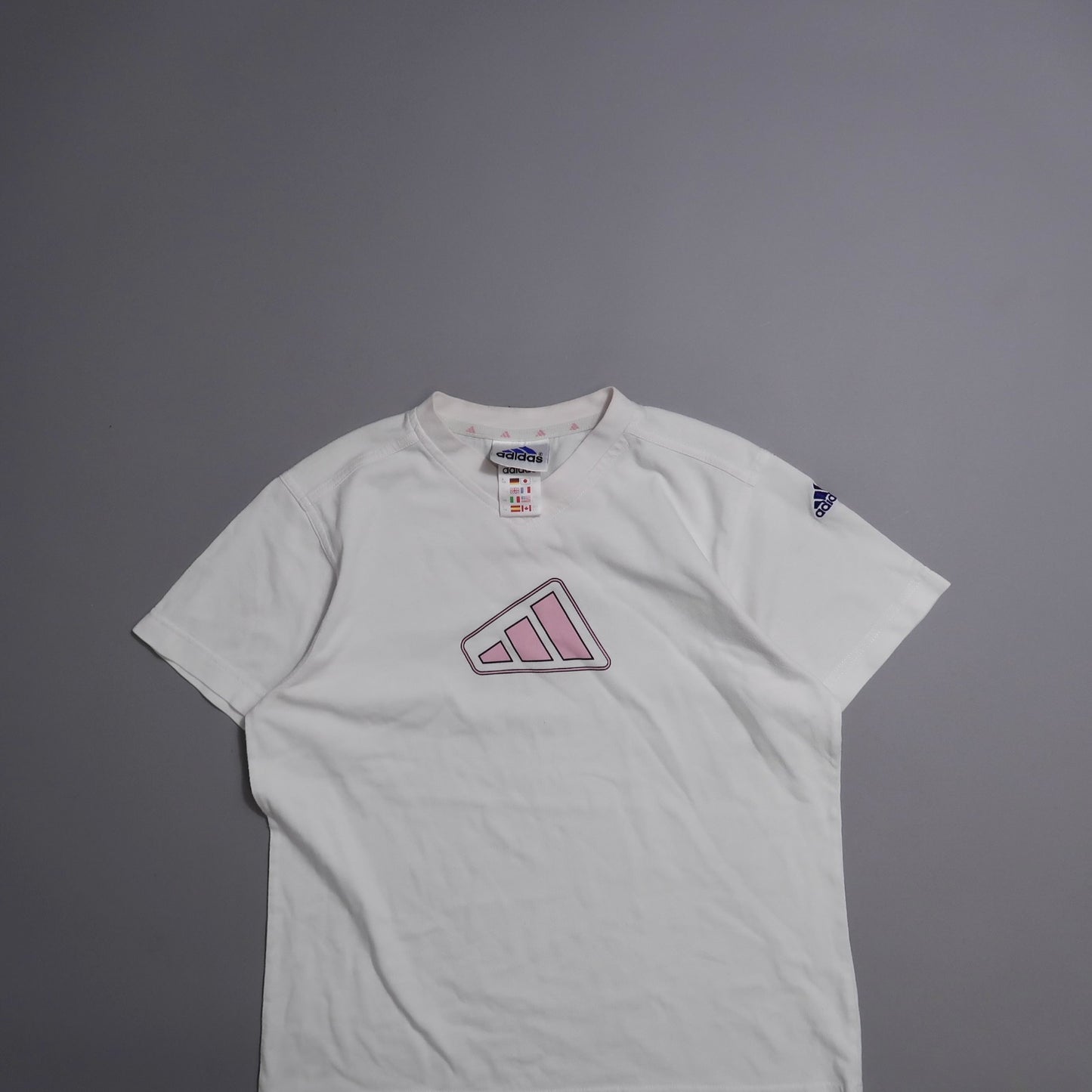 White Adidas shirt with pink logo on gray background.