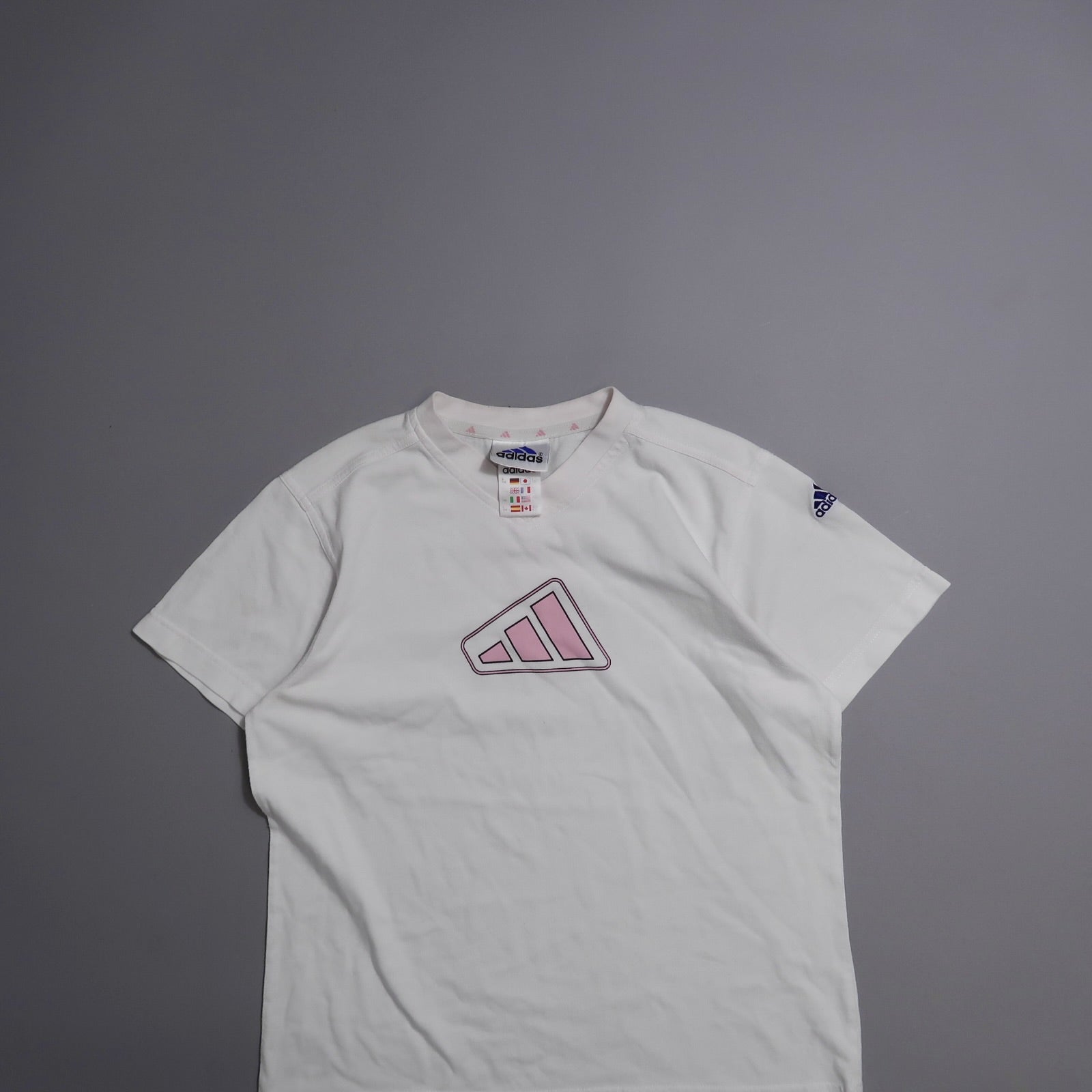 White Adidas shirt with pink logo on gray background.