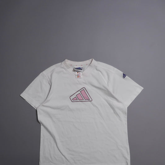 White Adidas shirt with pink logo on gray background.