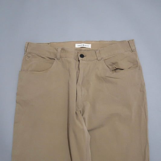 Beige pants with a button closure and front pockets on a gray surface.