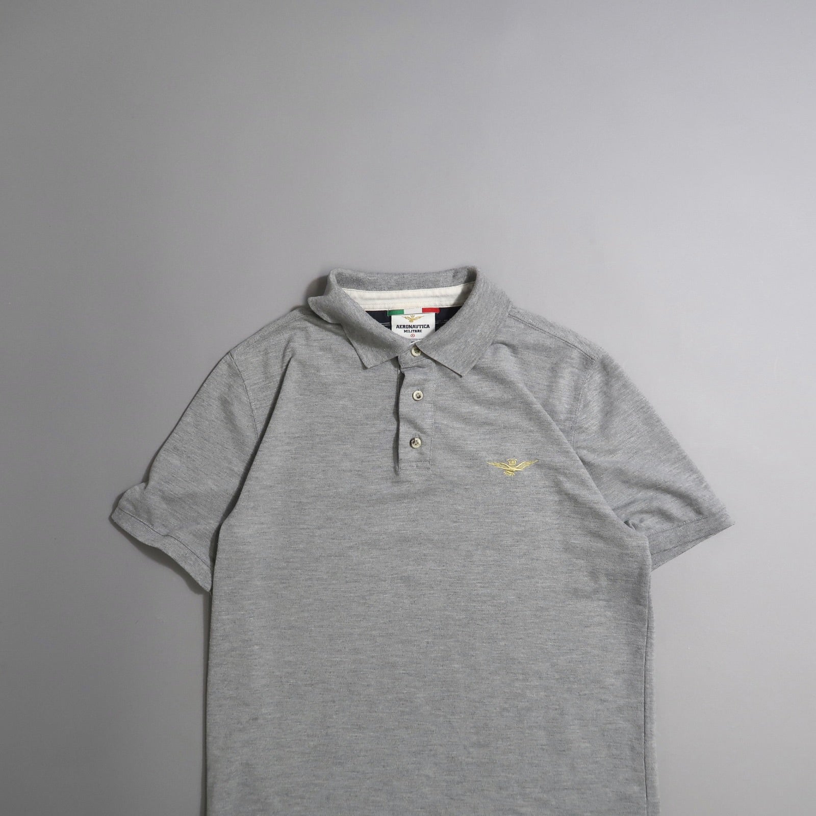 Gray polo shirt with emblem, laid flat on a gray background.