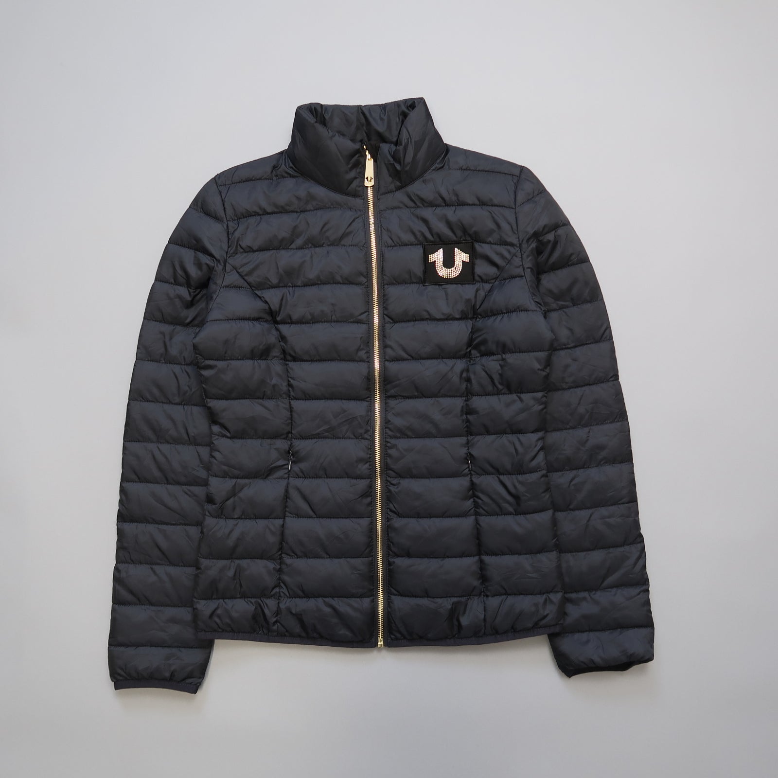 Black quilted jacket with a gold zipper and logo on the chest.