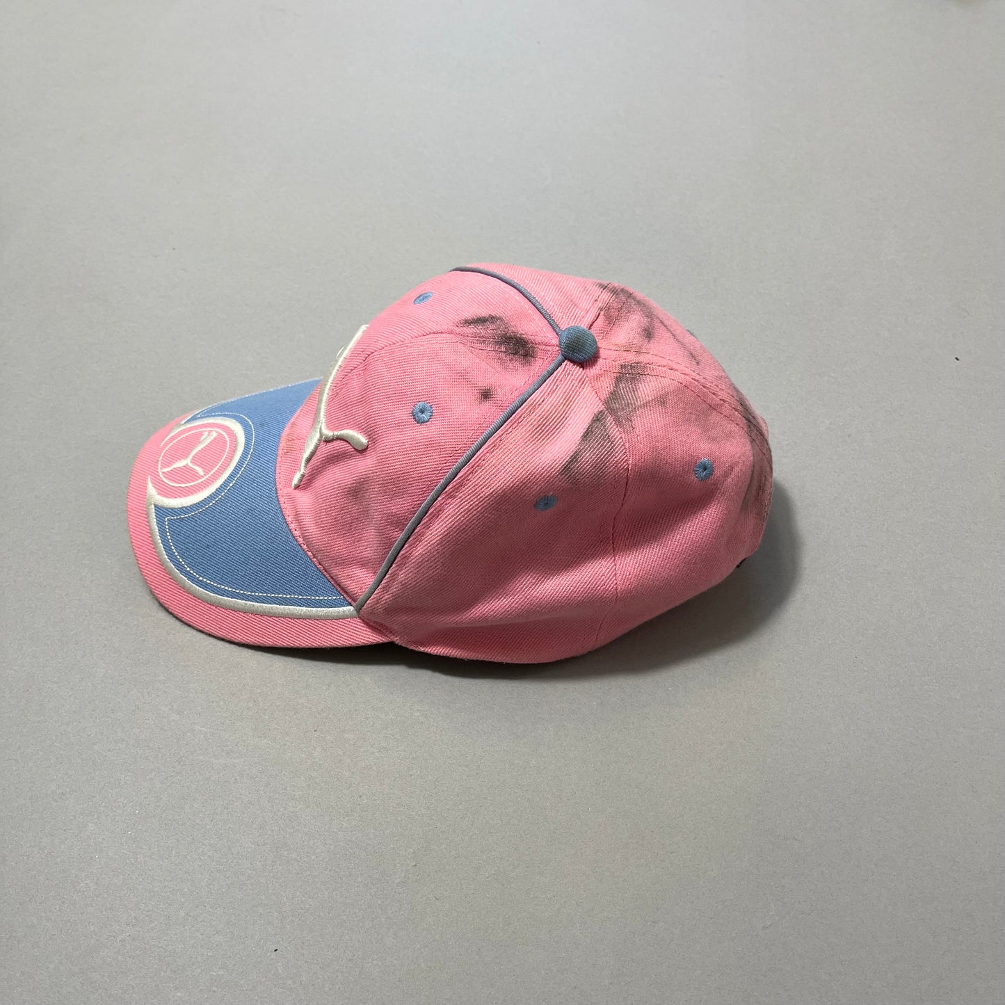 Pink and blue cap with logos, stained on top, on a gray surface.