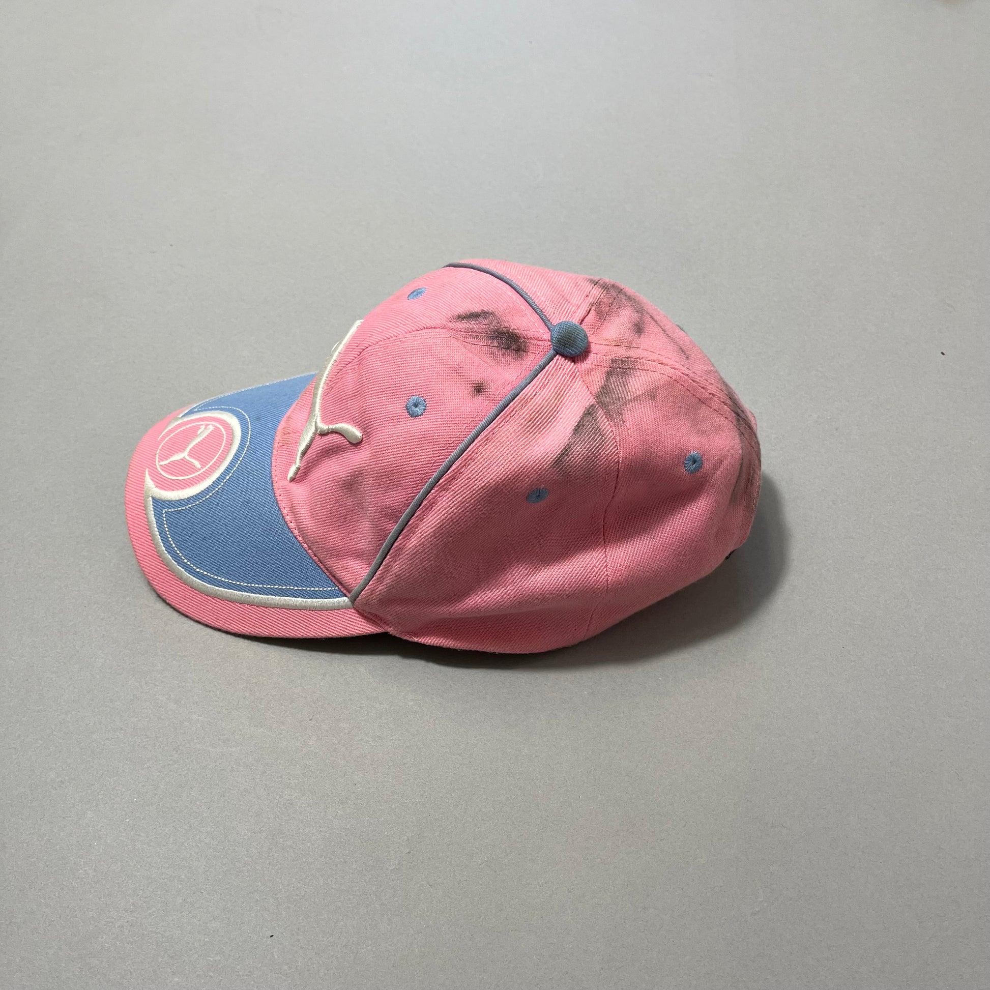 Pink and blue cap with logos, stained on top, on a gray surface.