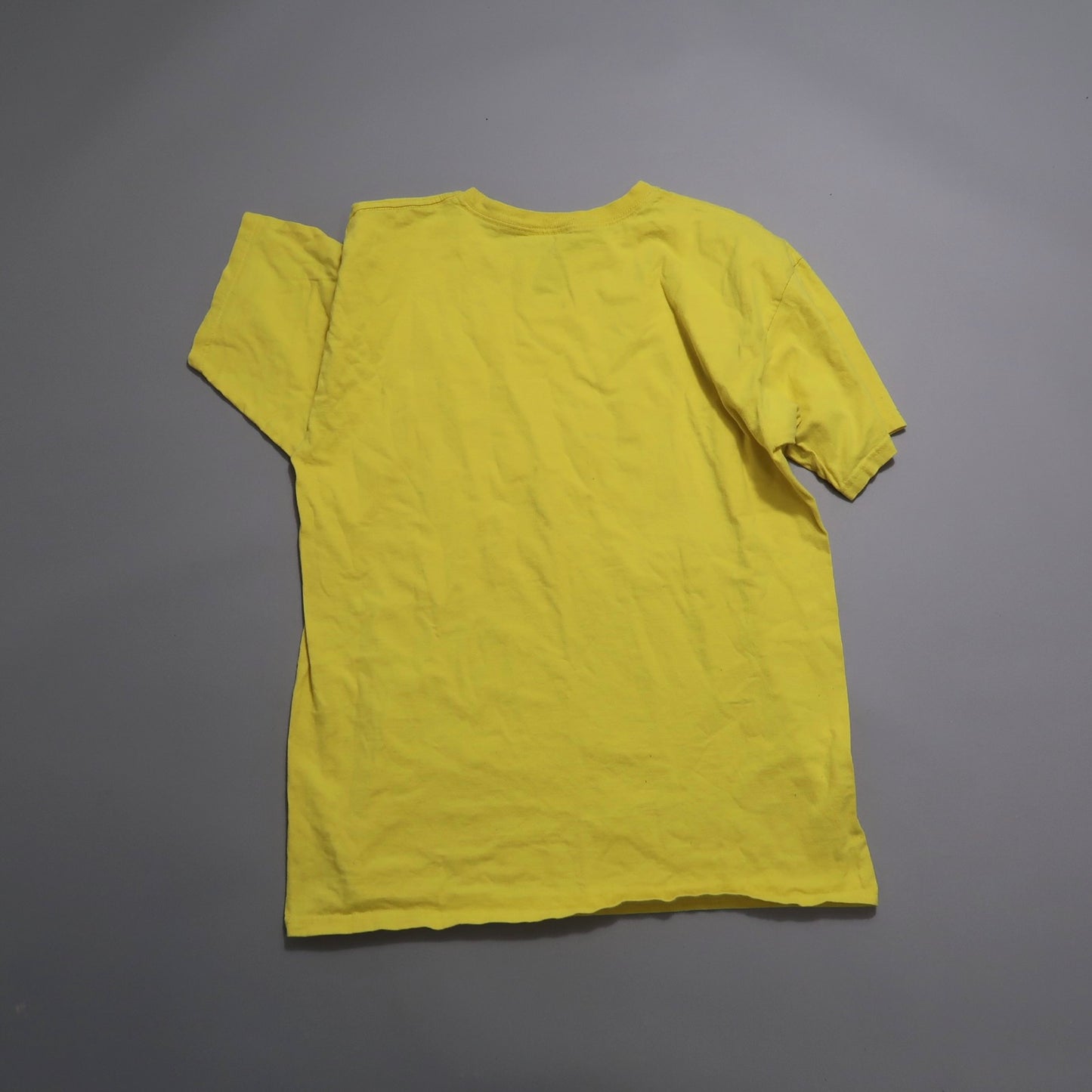 Yellow T-shirt laid flat on a gray background.