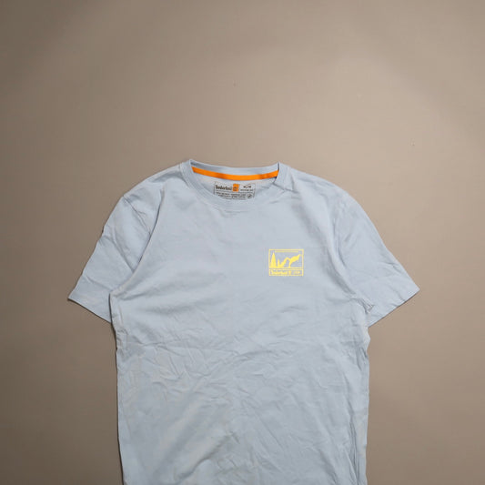 Light blue T-shirt with yellow logo on beige background.