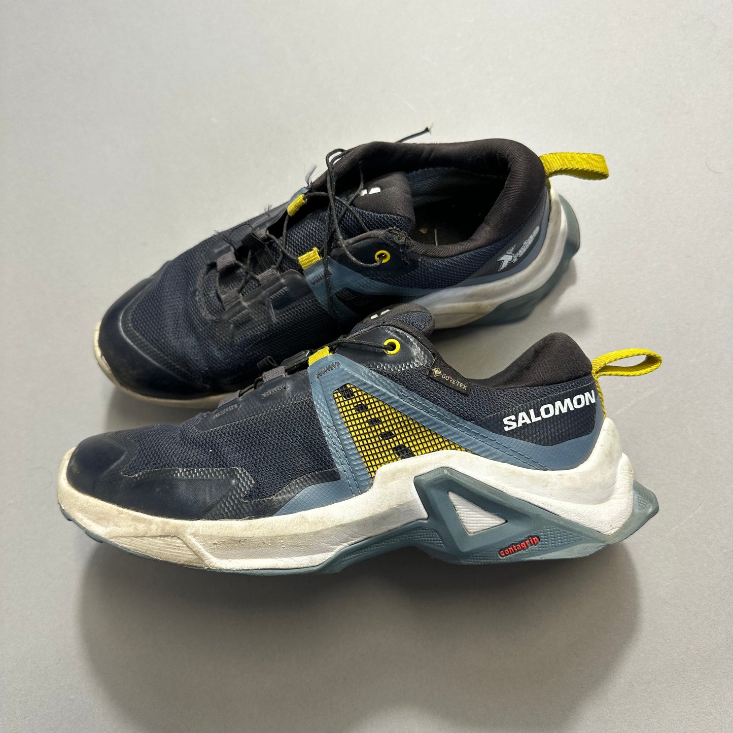 Black and yellow Salomon trail running shoes on a gray surface.