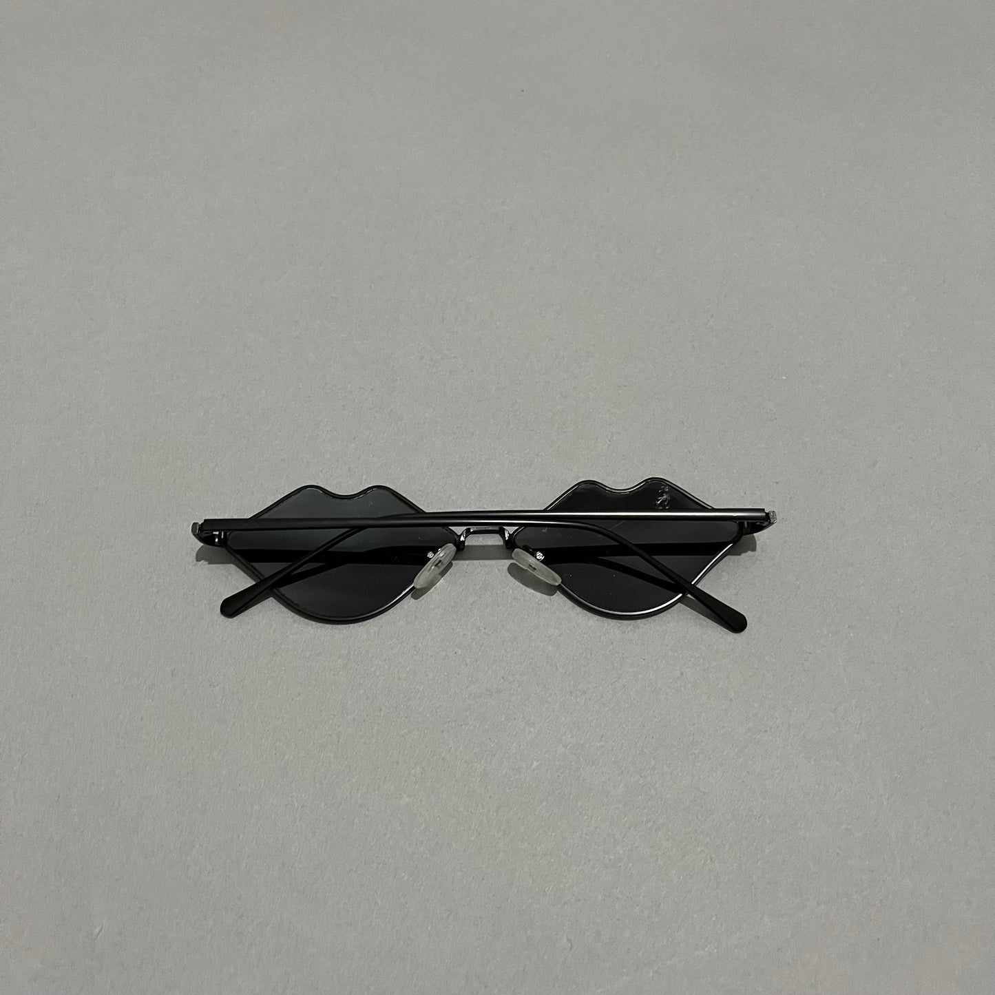 Sunglasses with lips-shaped lenses on a plain gray background.