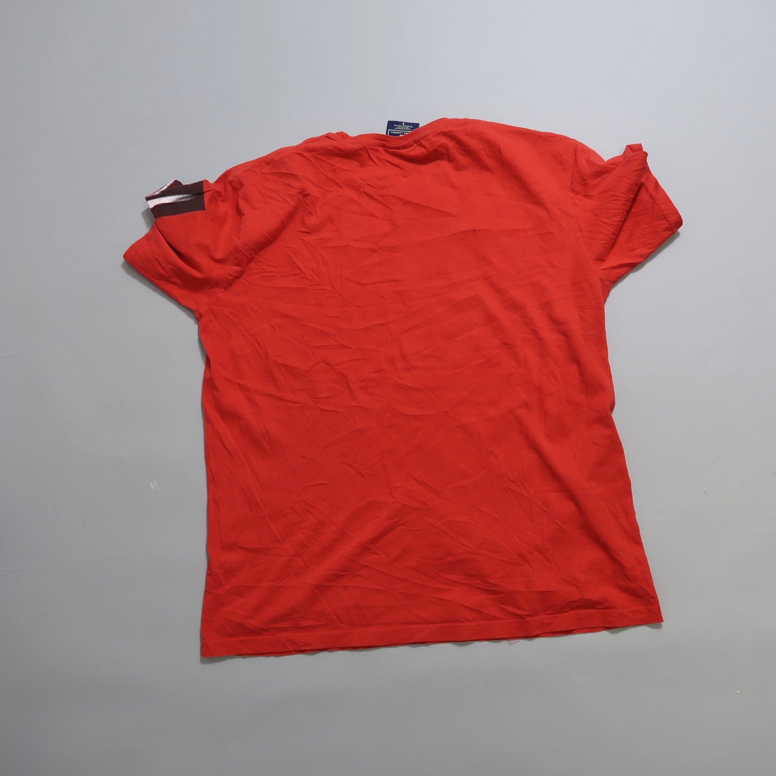 Red T-shirt lying flat on a grey surface.