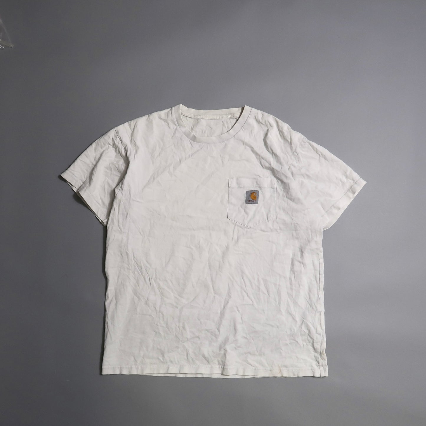 White T-shirt with a front pocket and logo on a gray background.