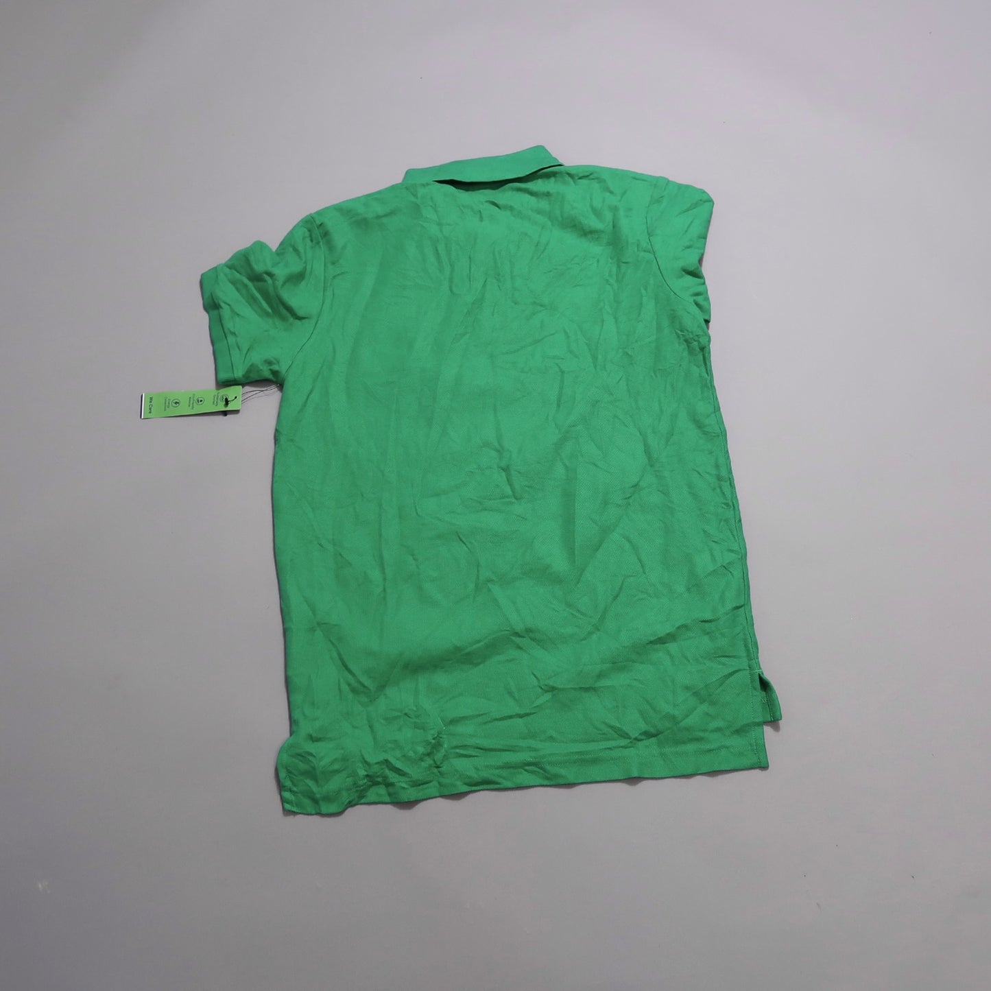 Green polo shirt laid flat with a tag attached.
