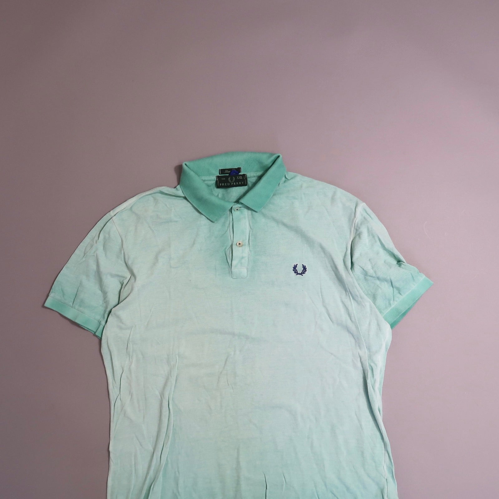 Light green polo shirt with a small embroidered logo on a gray background.