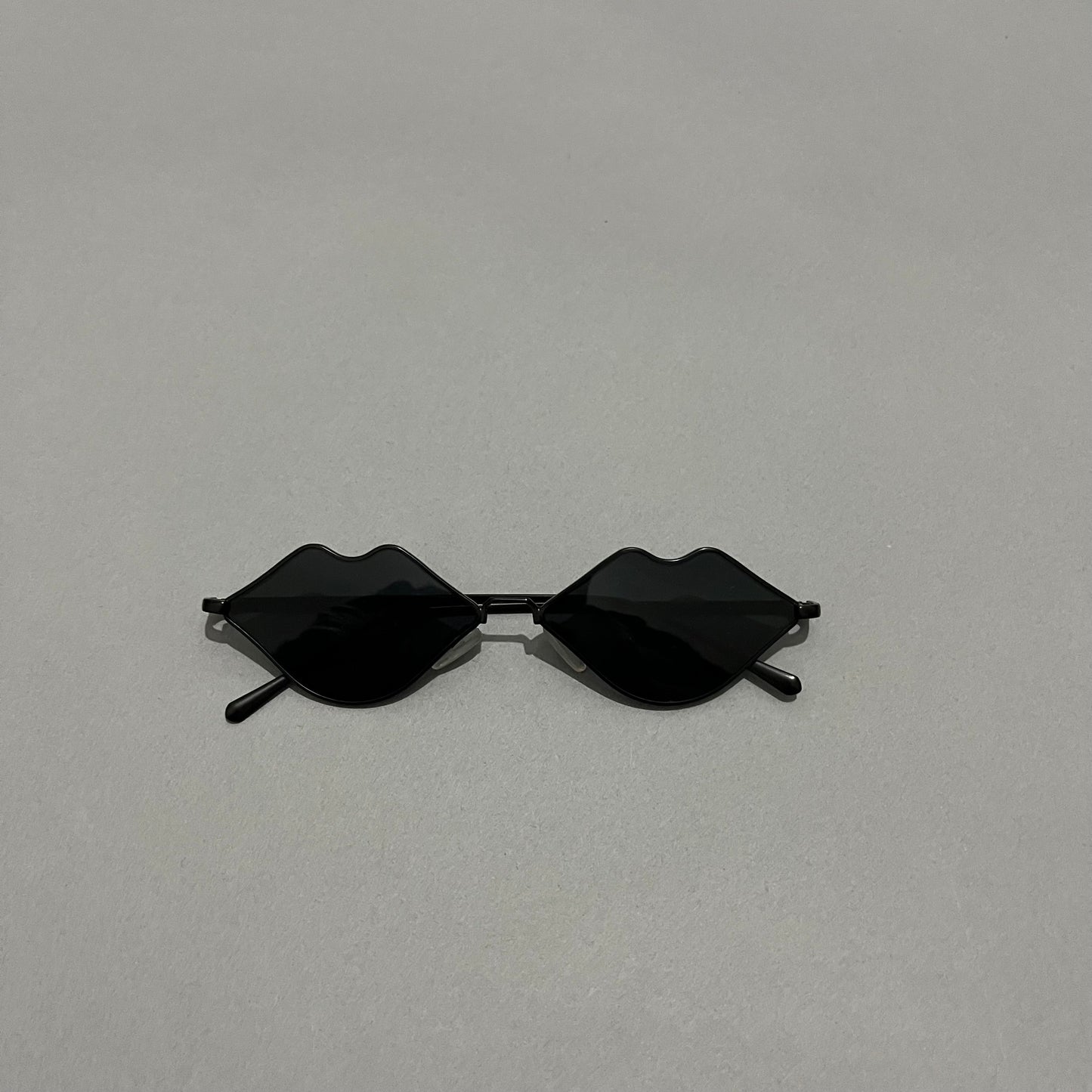 Black sunglasses with lenses shaped like lips on a gray background.