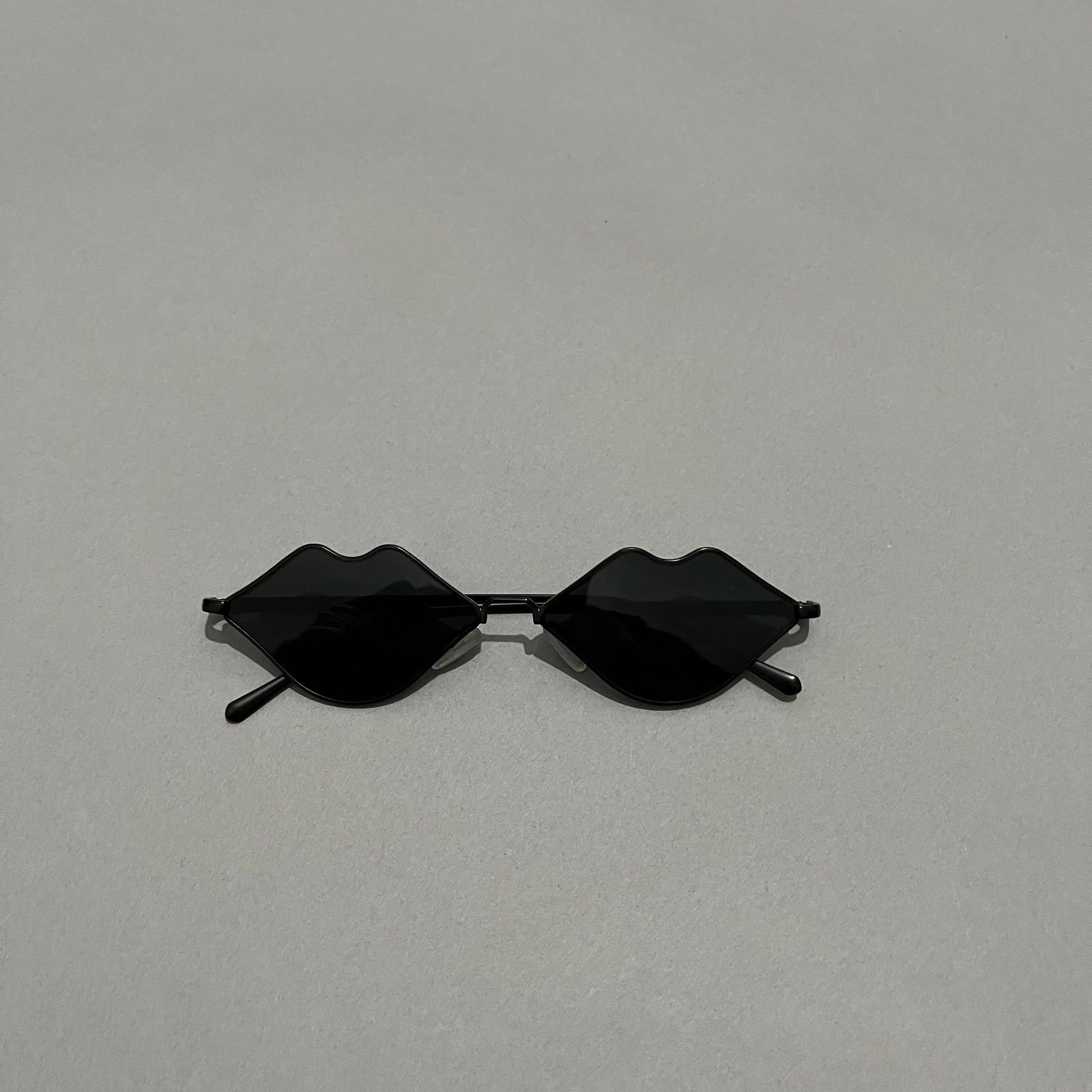Black sunglasses with lenses shaped like lips on a gray background.