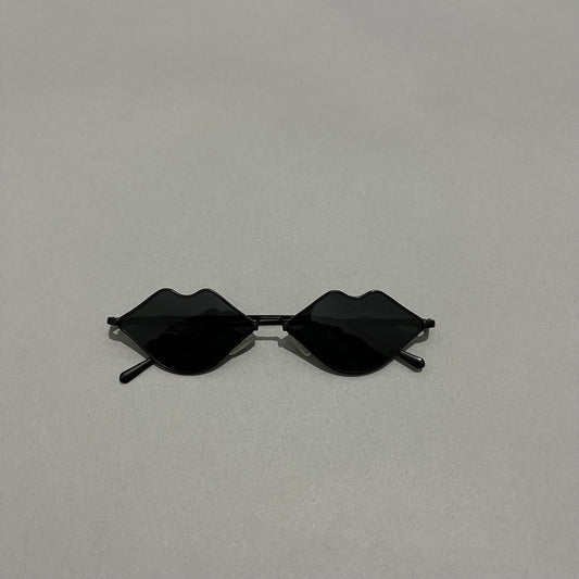 Black sunglasses with lenses shaped like lips on a gray background.