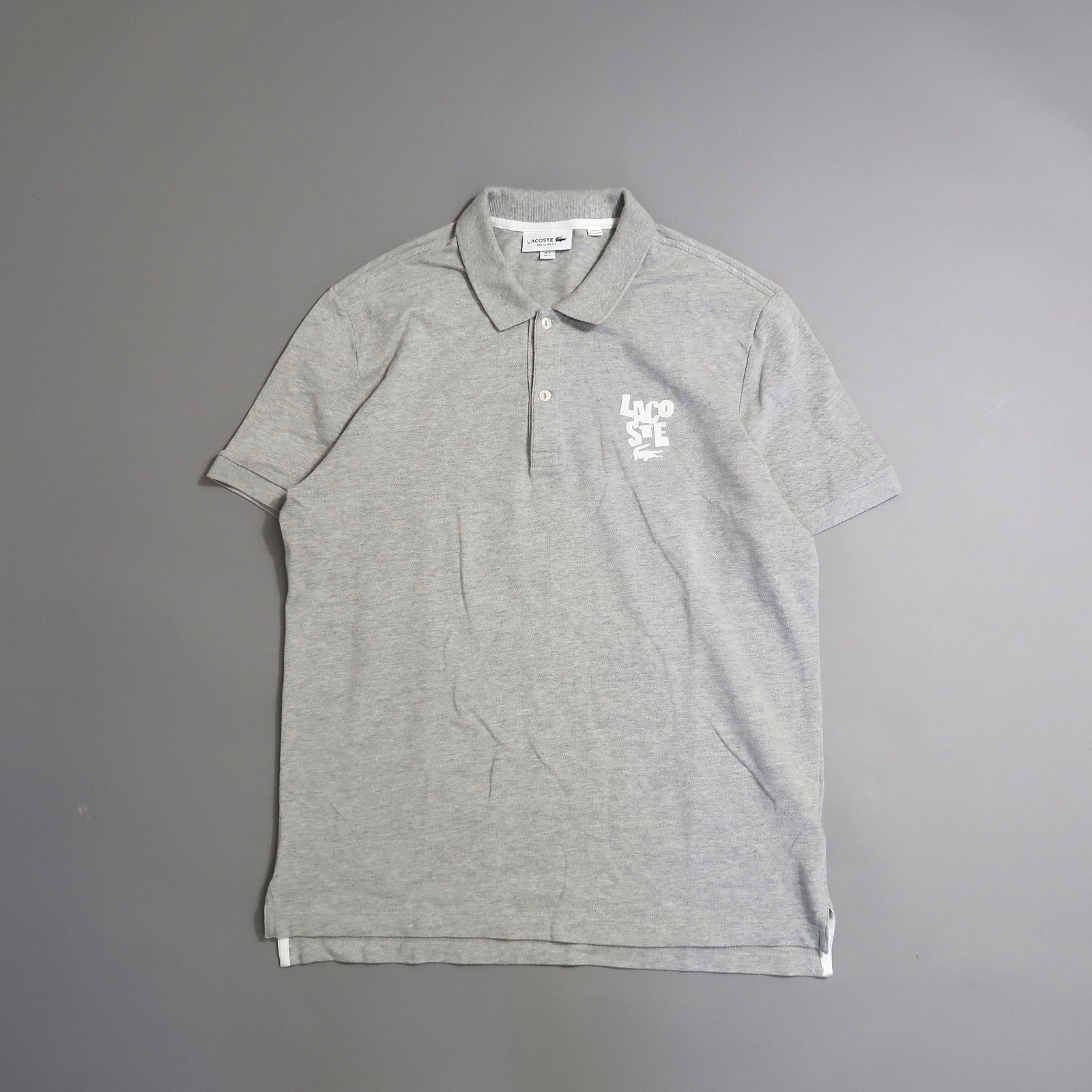 Gray polo shirt with a logo on the upper left chest on a gray background.