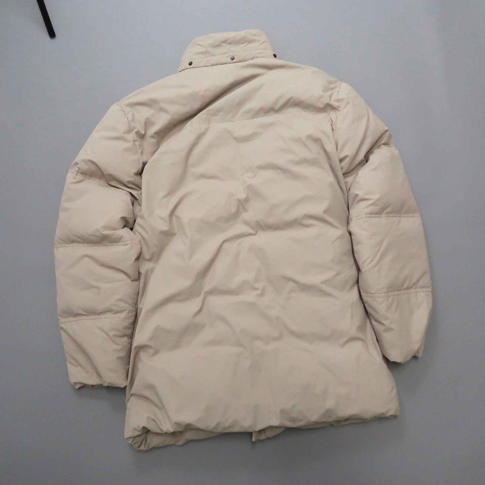 Beige puffer coat laid flat on a gray surface.