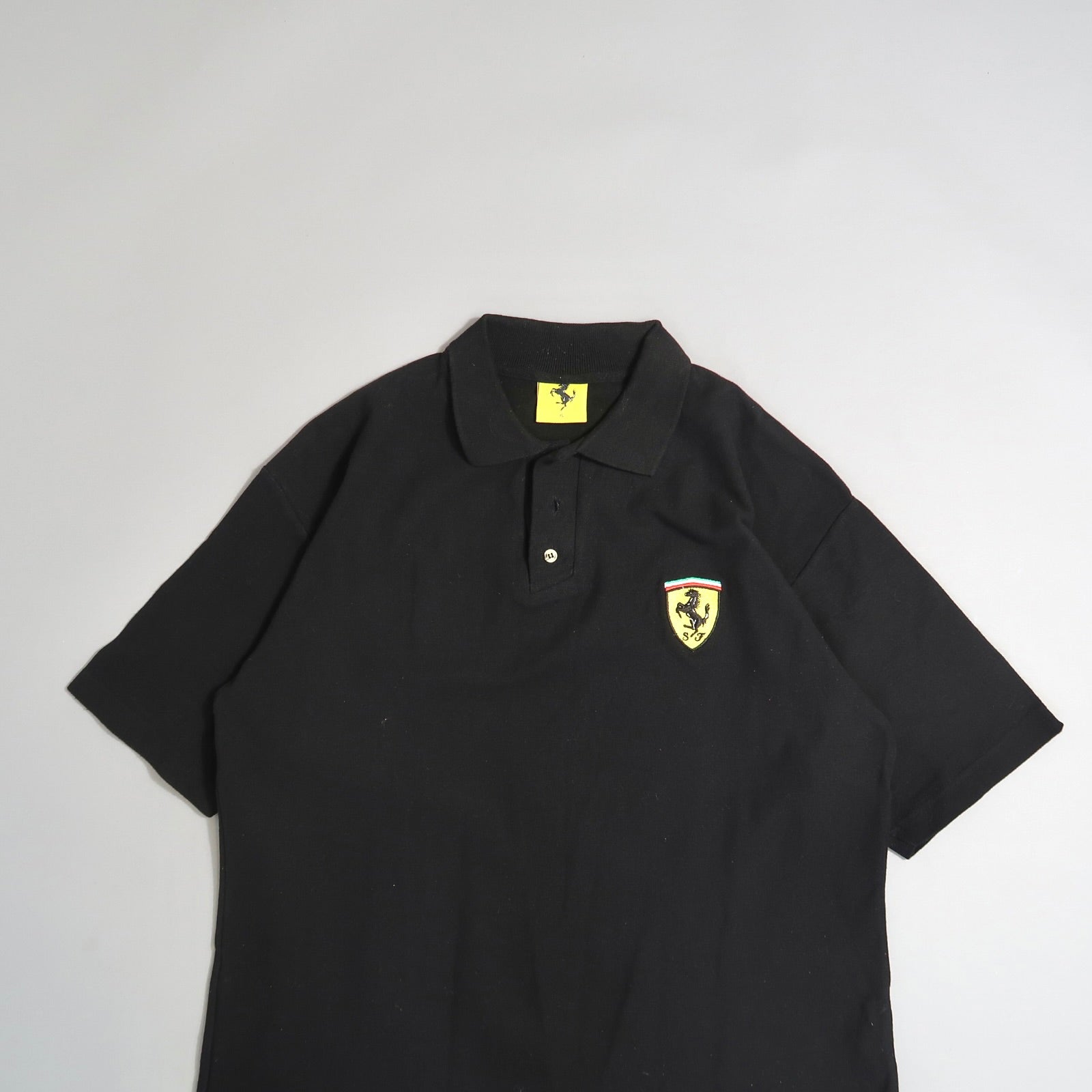 Black polo shirt with a yellow logo patch on the left chest.
