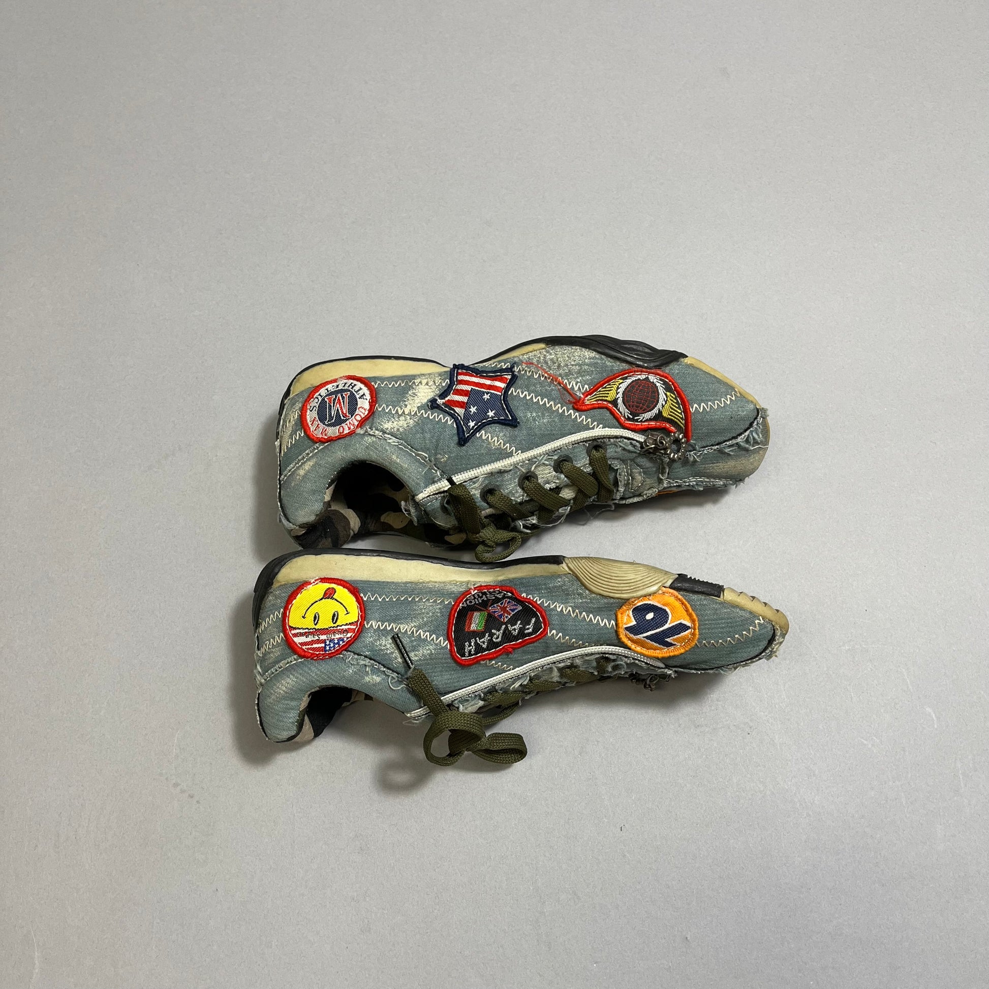 Worn sneakers with colorful patches on a gray background.