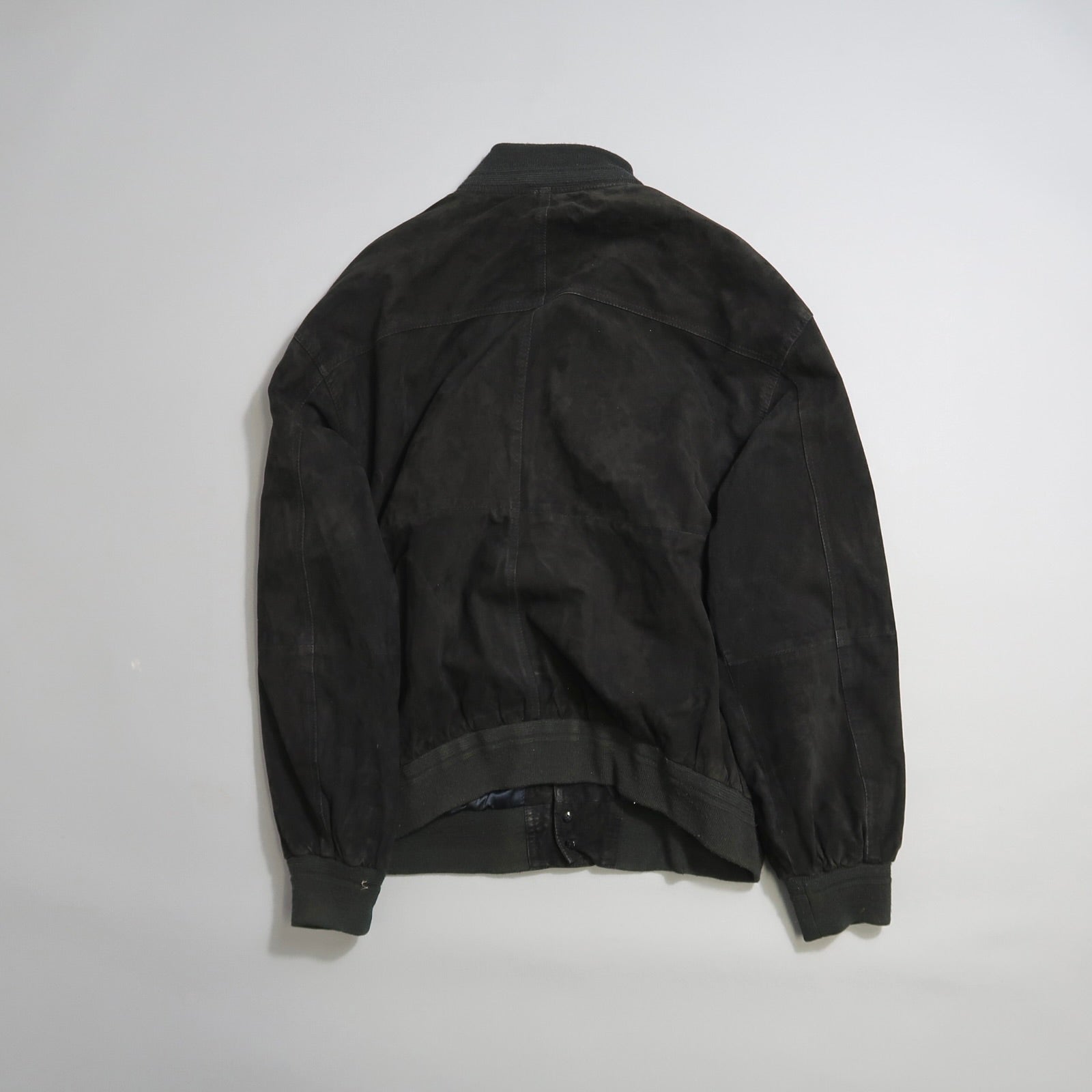 Back view of a black bomber jacket on a white background.