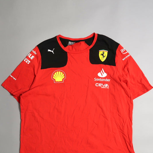 Red sports t-shirt with logos, including a Ferrari shield, on a gray background.