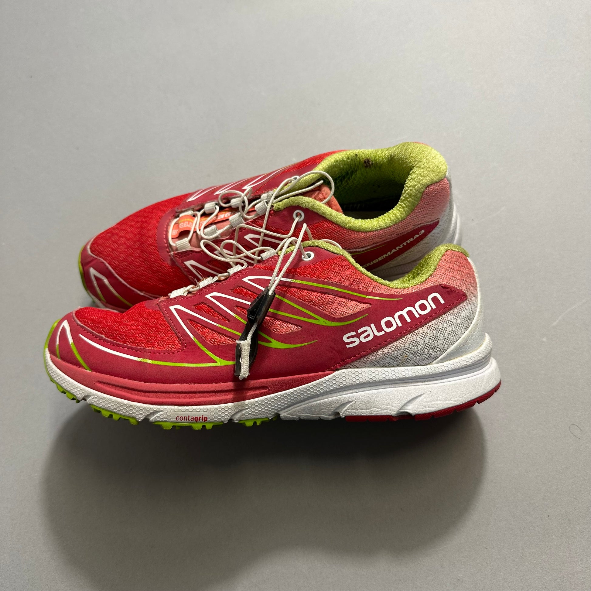 Red and green Salomon running shoes on a gray surface.