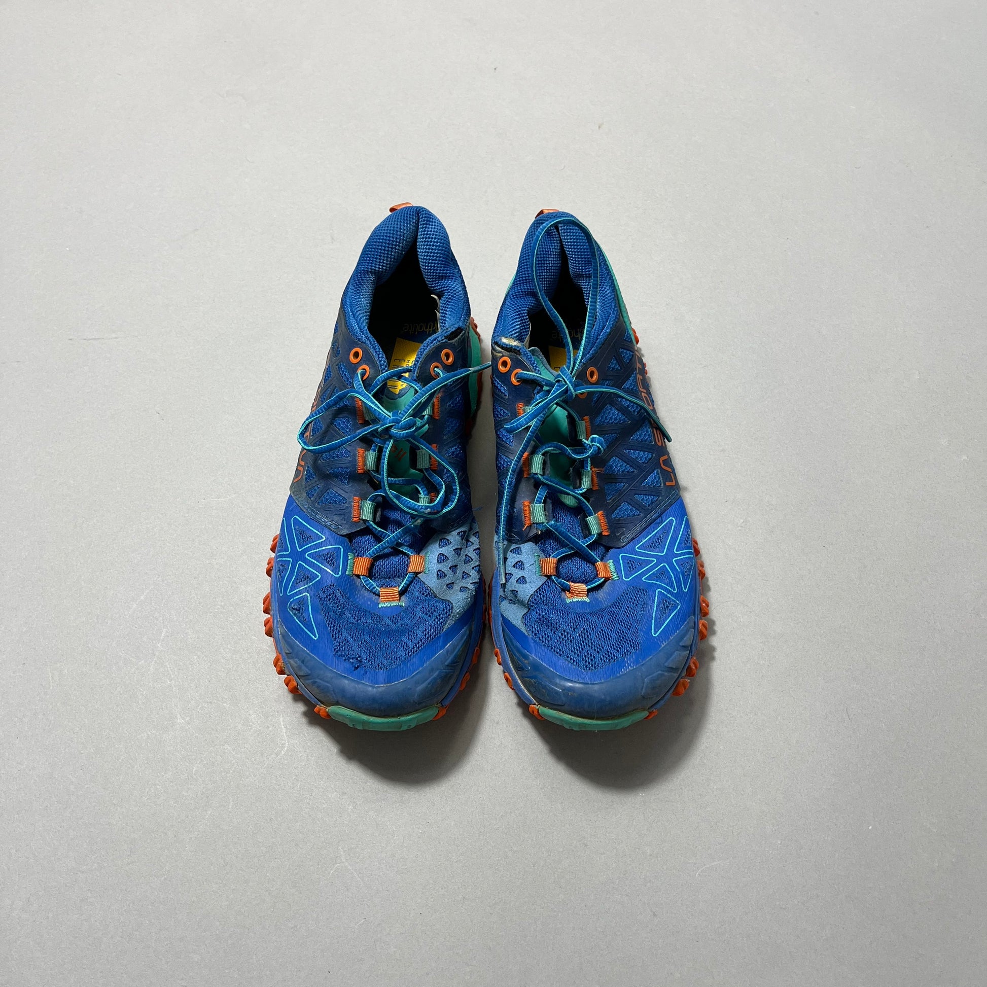 Blue and orange trail running shoes on a gray background.