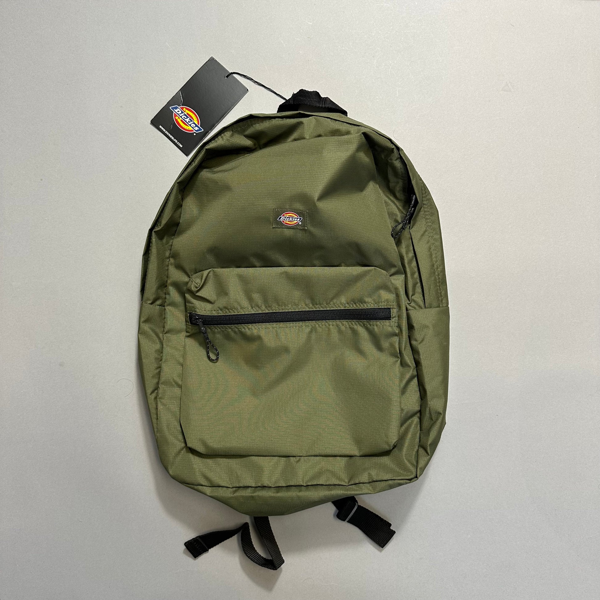 Green backpack with front pocket and tag attached on a light background.